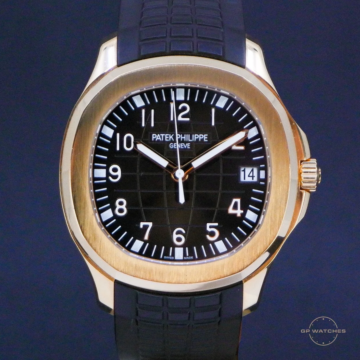 A men's luxury wristwatch with a black dial, gold bezel, and black rubber strap, displaying the time as 10:07 and the date as the 14th.