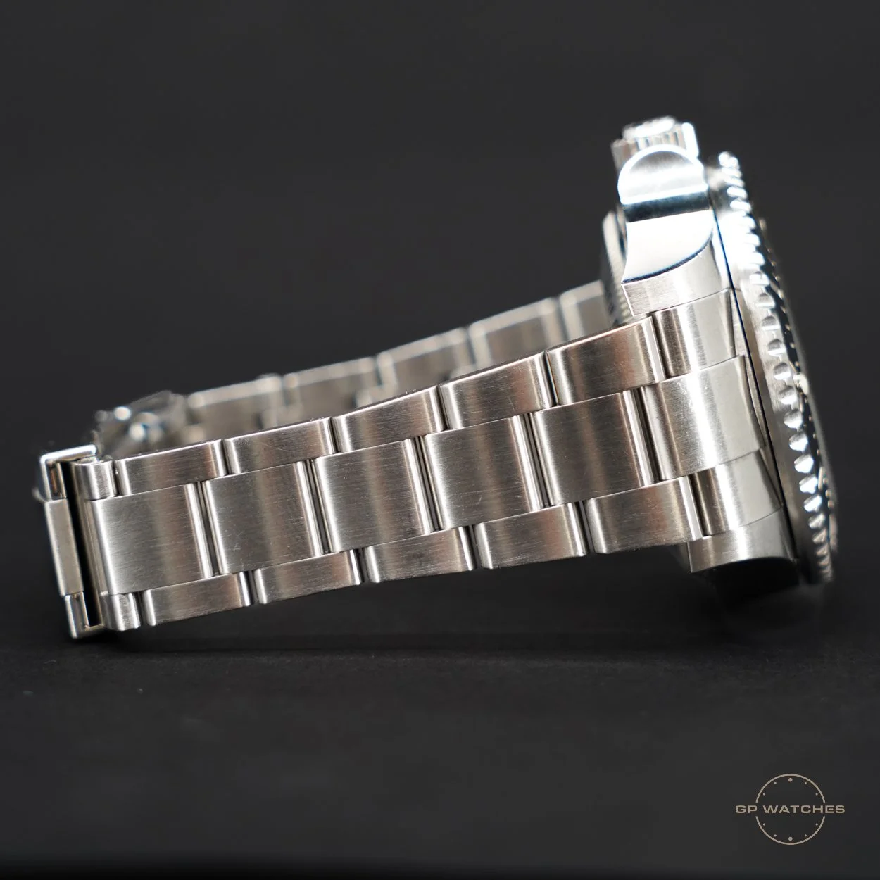 Close-up of a silver metal wristwatch with a brushed metal band and a fluted bezel, lying on a black background.
