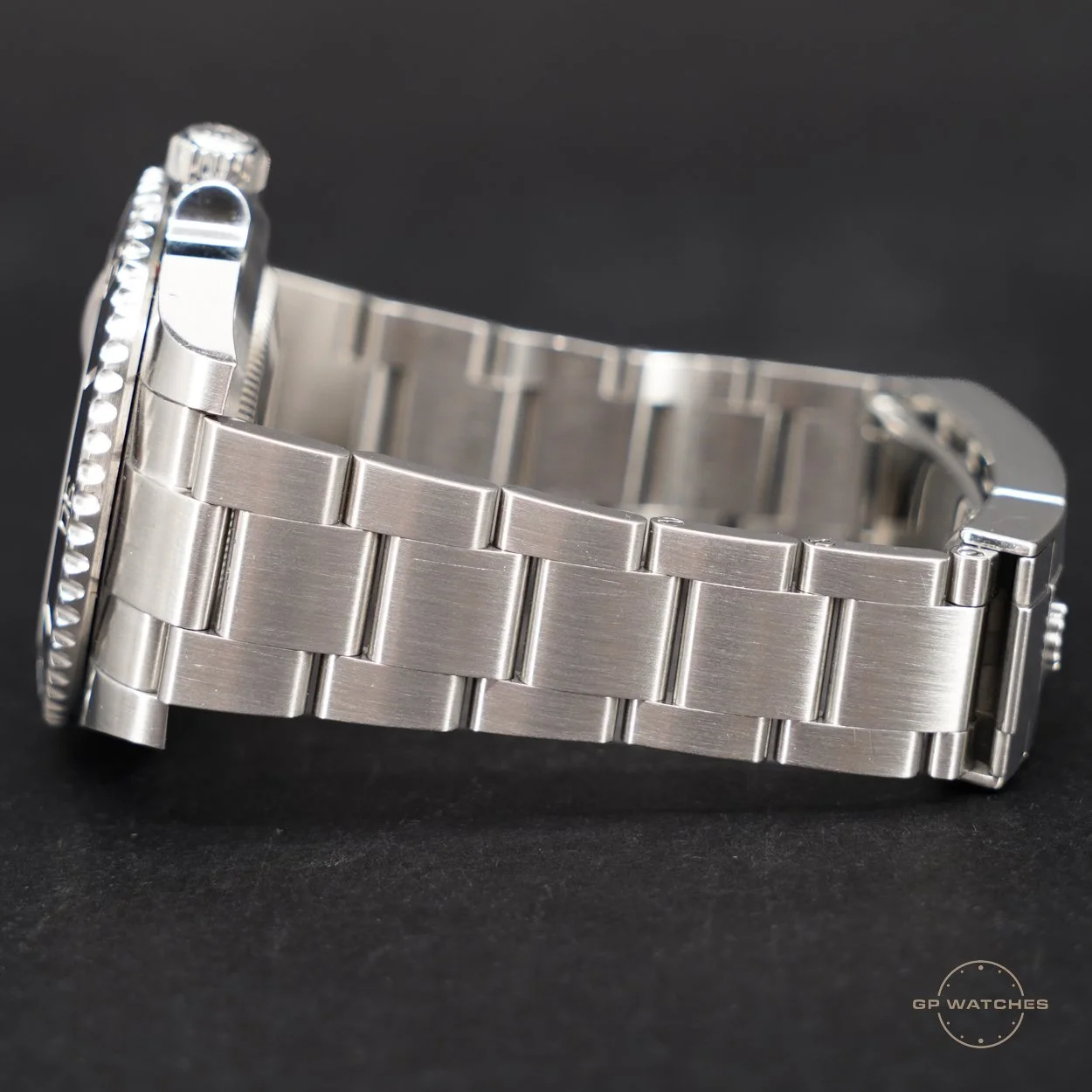 Close-up of a stainless steel watch band with a portion of the watch face visible, set against a black background.