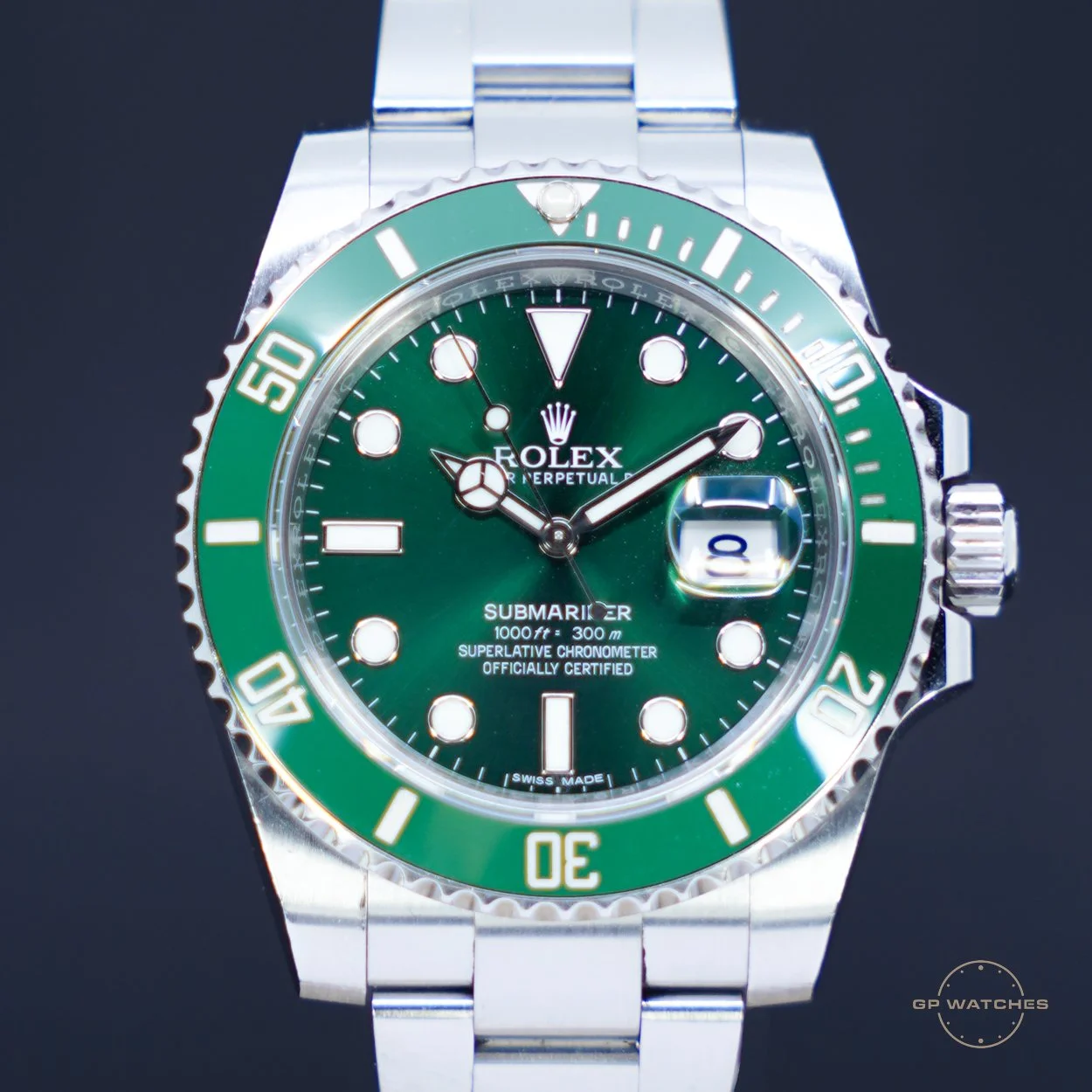 A close-up of a Rolex Submariner watch with a green bezel and dial, silver metal bracelet, and a date window showing the number 8.