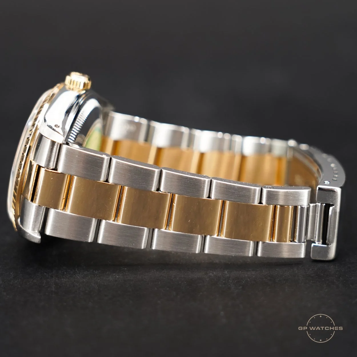 Close-up of a wristwatch with a two-tone metal band, featuring silver and gold links, against a black background.