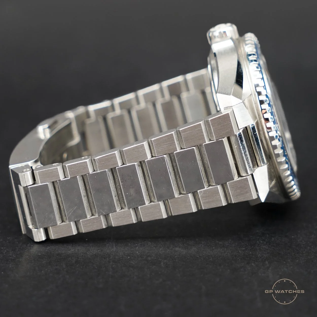 Close-up of a stainless steel wristwatch with a metal link bracelet, partially visible dial, and bezel, placed on a black background.
