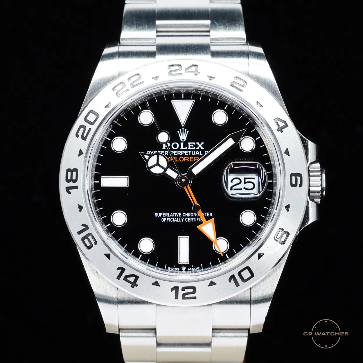A Rolex Explorer II wristwatch with a black face, silver bezel, and stainless steel band. It has a date window at 3 o'clock and orange accents on the hour hand and second hand, with the text "Explorer" and
