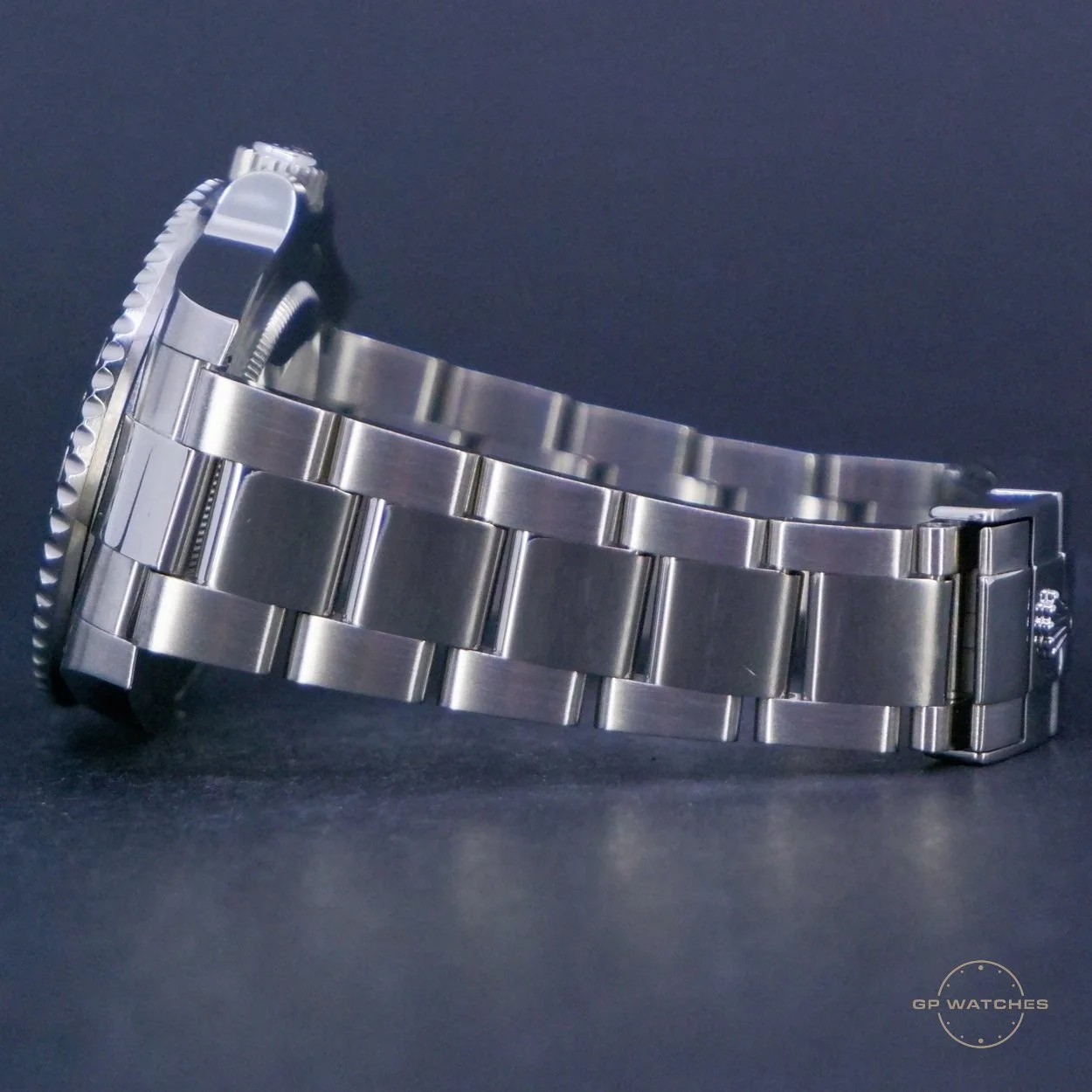 A stainless steel wristwatch with a metal bracelet band and a fluted bezel, placed on a dark background.