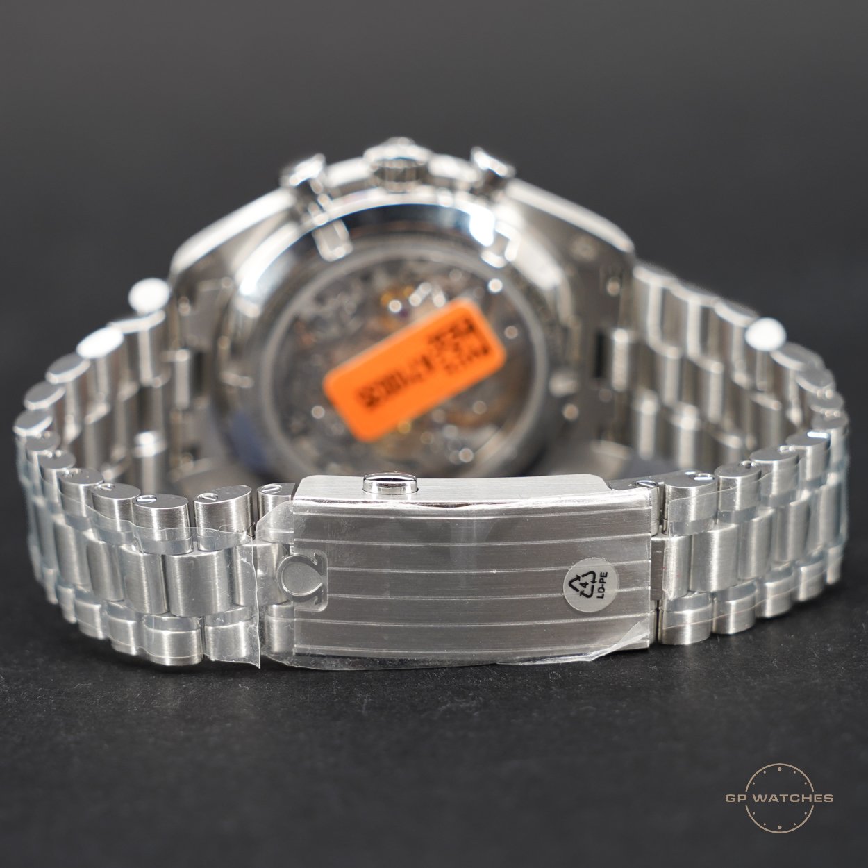 Close-up of the back of a silver wristwatch with a metal bracelet, showing the transparent case back and a warning sticker.