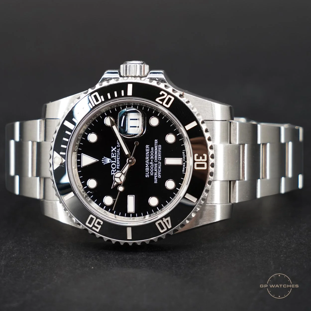 a stainless steel Rolex Submariner watch with a black dial and bezel, large luminous markers, and a date window with magnification at 3 o'clock, resting on a black surface.