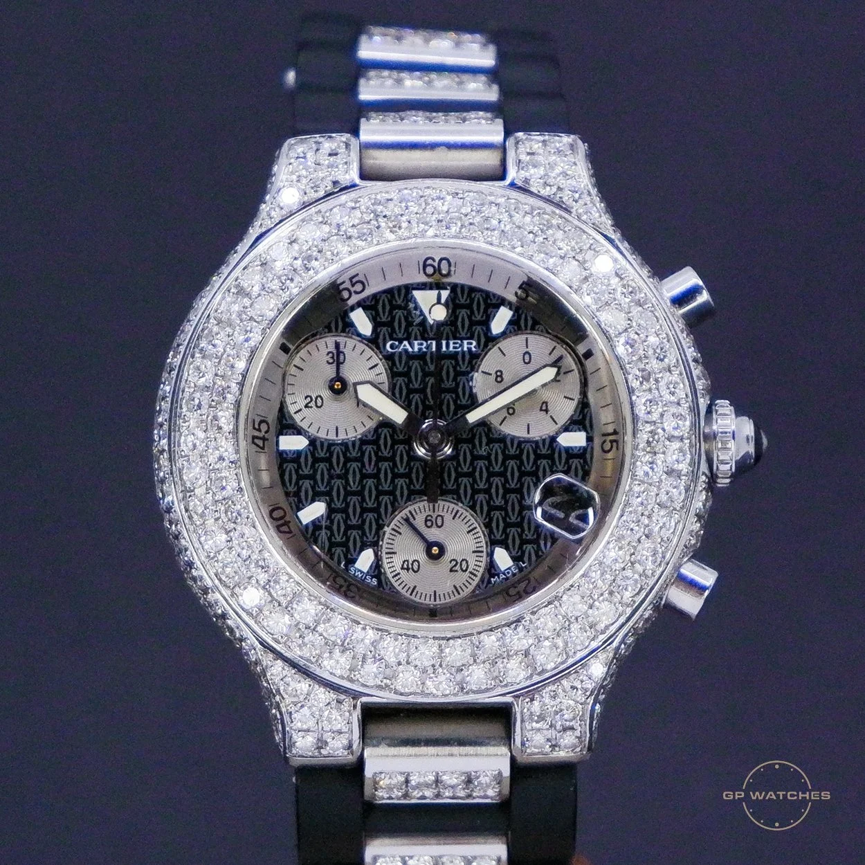 A luxury wristwatch with a diamond-encrusted bezel and band, black textured dial, three subdials, and a date window, displaying the brand name 'Cartier'.