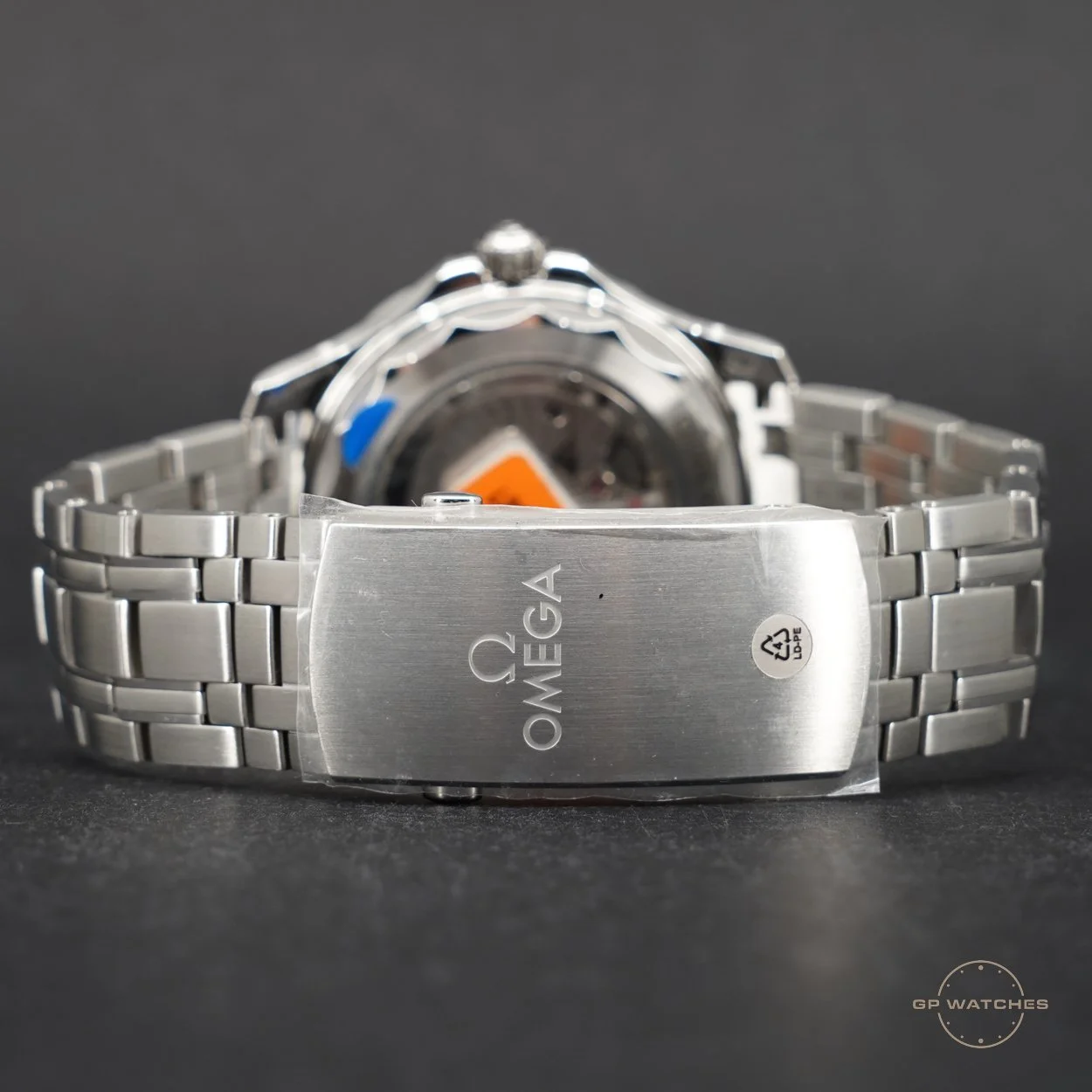 Close-up of a stainless steel Omega wristwatch with a metal bracelet on a dark surface, showing the back of the watch and engraved Omega logo.