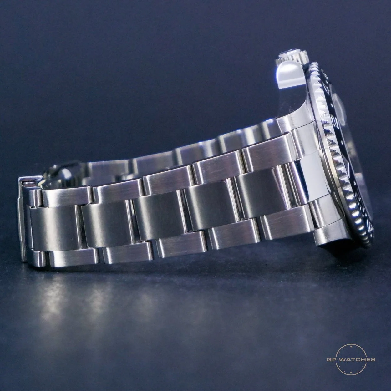 Silver wristwatch with metal band resting on a dark surface, view from the side showing the watch face and band links.