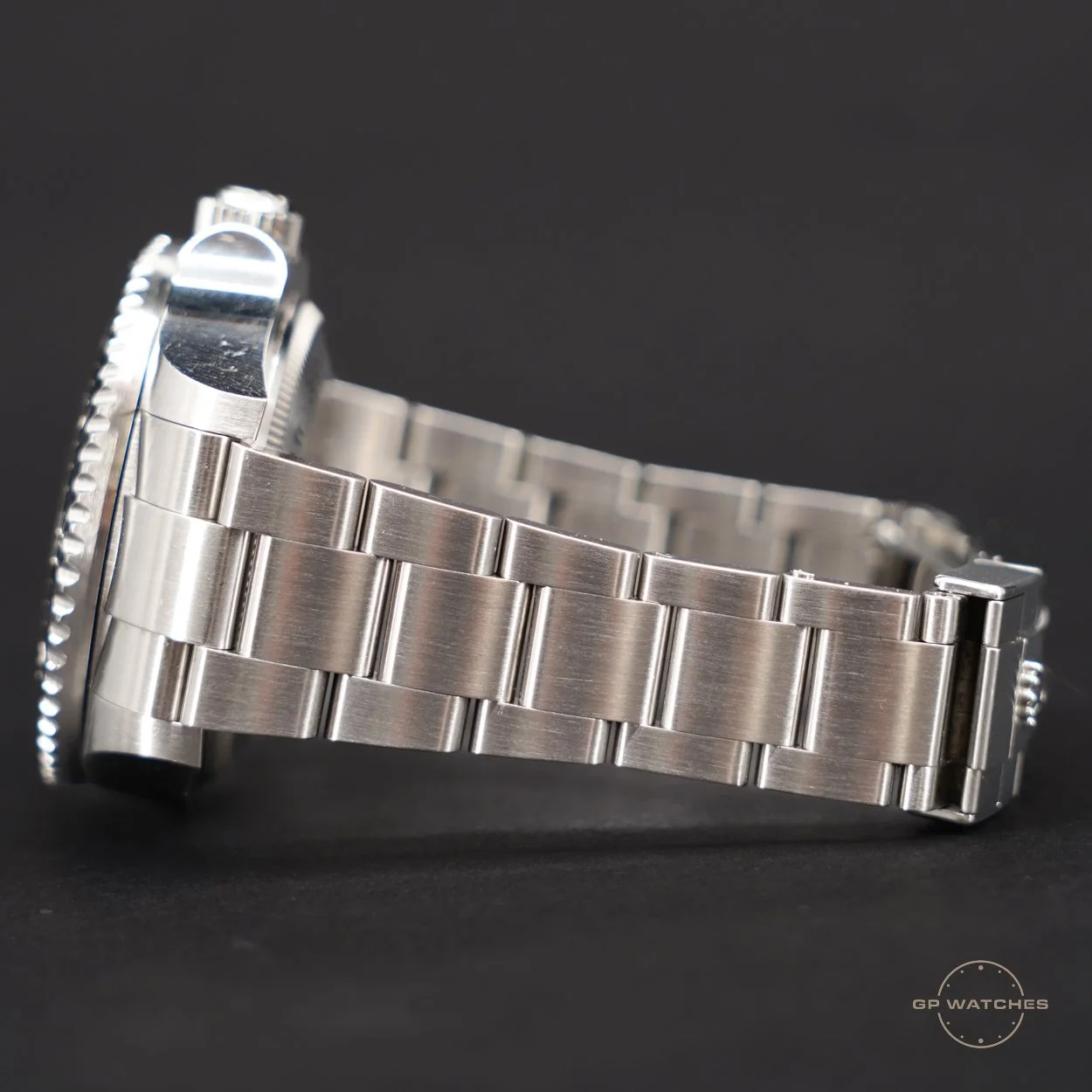 Close-up side view of a silver metallic wristwatch with a metal bracelet and a textured bezel, set against a dark background.