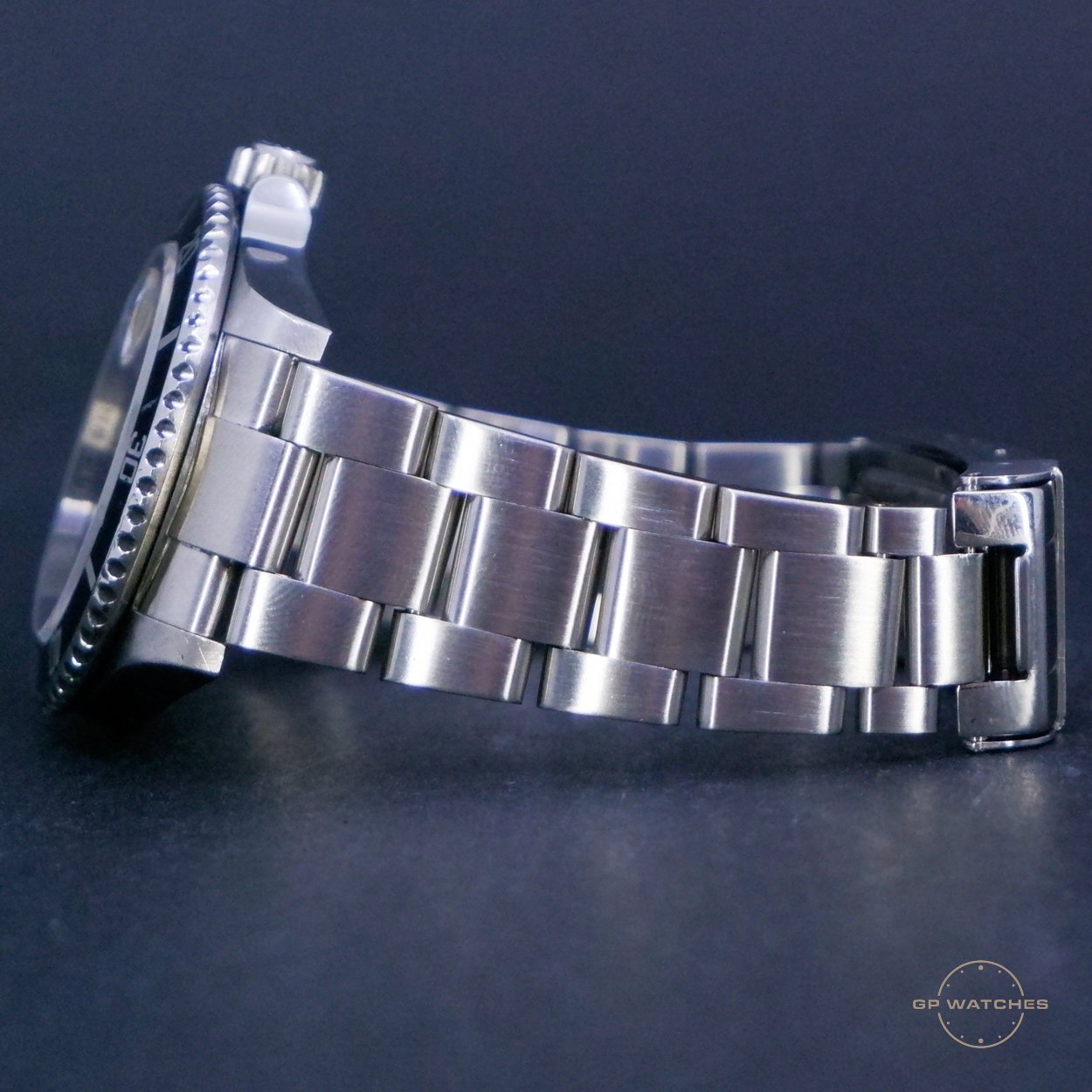 Side view of a silver stainless steel wristwatch with a metal link band, placed on a dark surface.