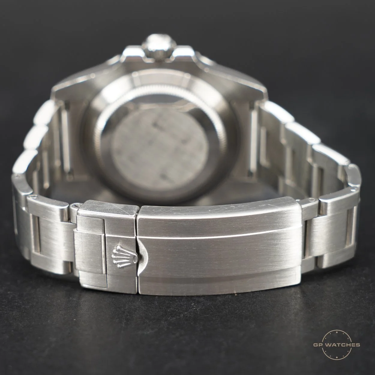 The back of a silver Rolex wristwatch with a metal bracelet and a closed clasp, displaying the Rolex crown logo on the clasp.
