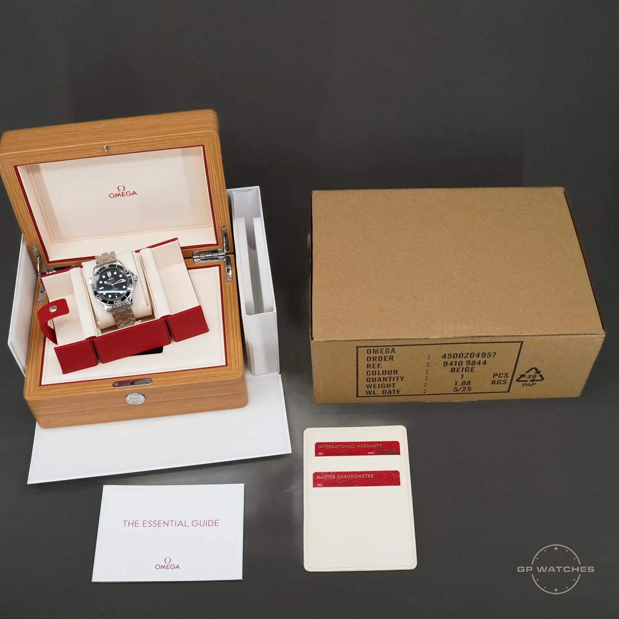 Omega wristwatch in a wooden box, with additional accessories and documentation, on a dark surface.