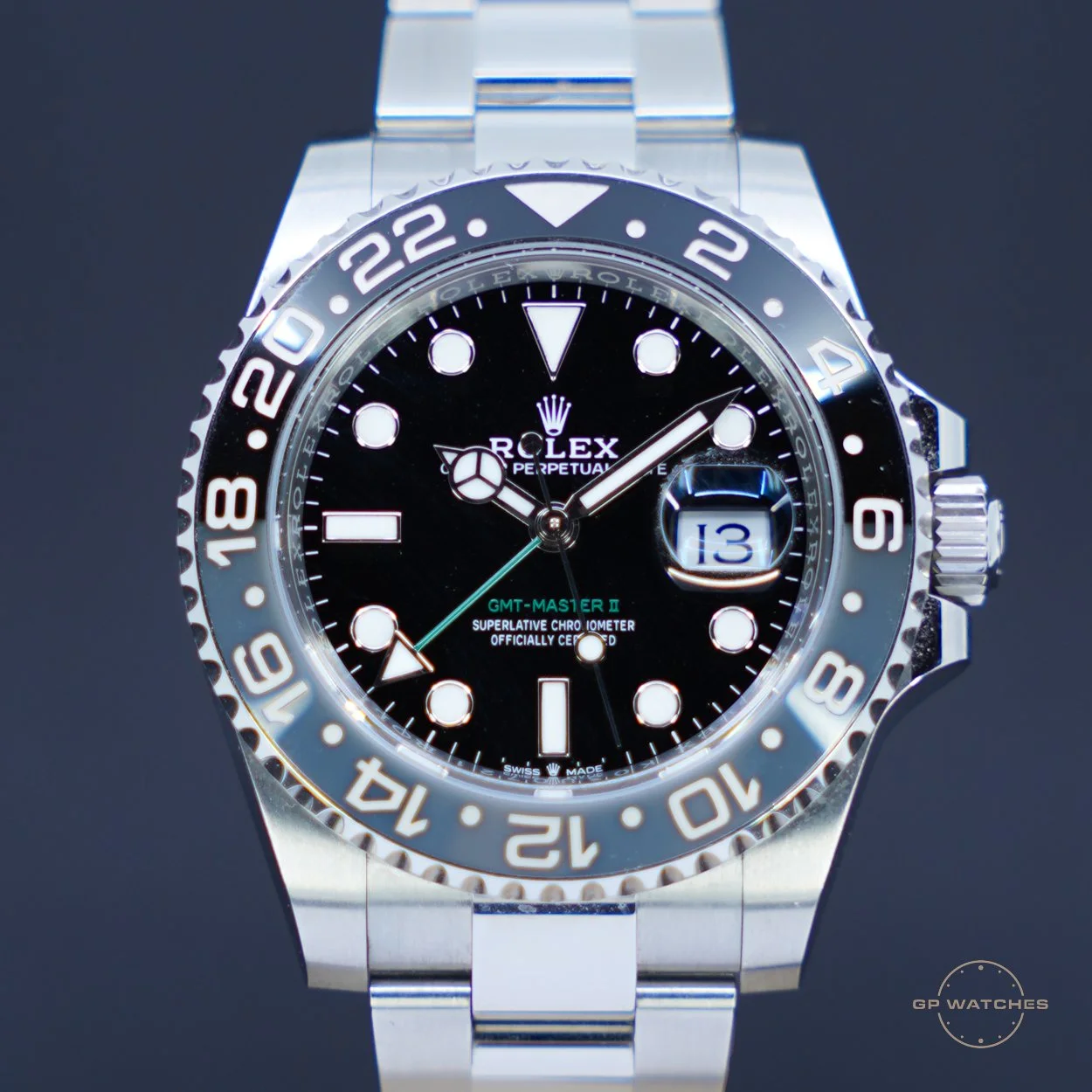 Close-up of a silver Rolex GMT-Master II watch with a black dial, white hour markers, and a date window showing the 13th. The watch has a black and silver bezel with 24-hour markings, and a silver bracelet. The time displayed is approximately 8:10.