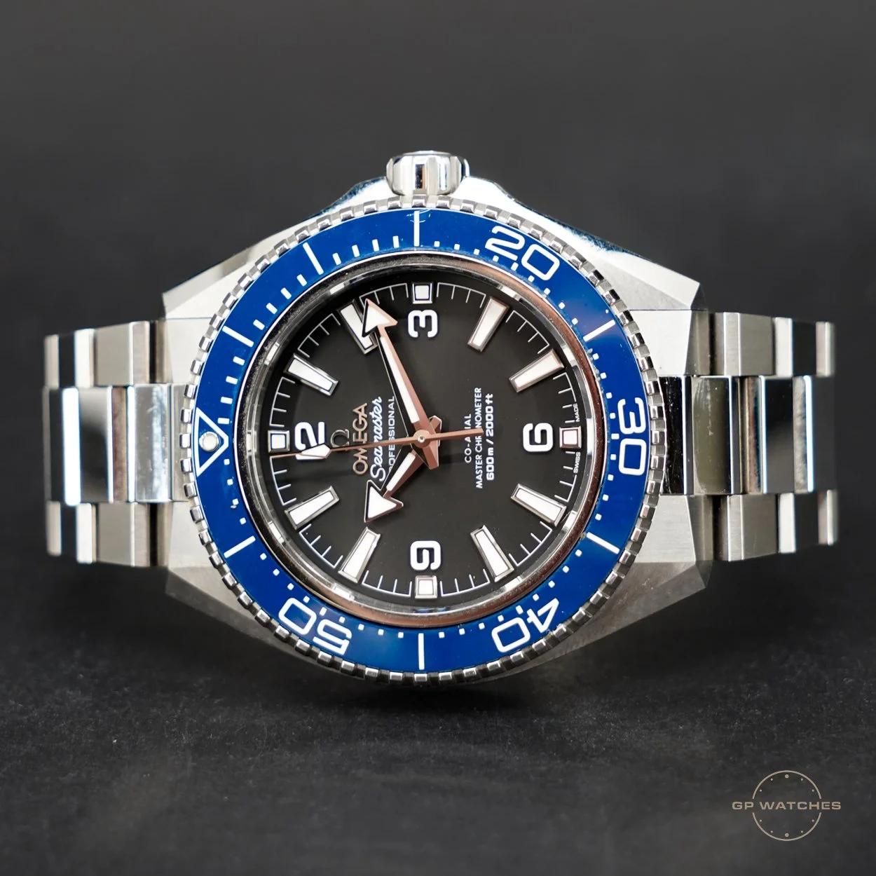 A close-up of a stainless steel Omega Seamaster professional diving watch with a black and blue bezel and black dial, featuring large white hour markers, luminous hands, and a date window at 6 o'clock, set against a dark background.