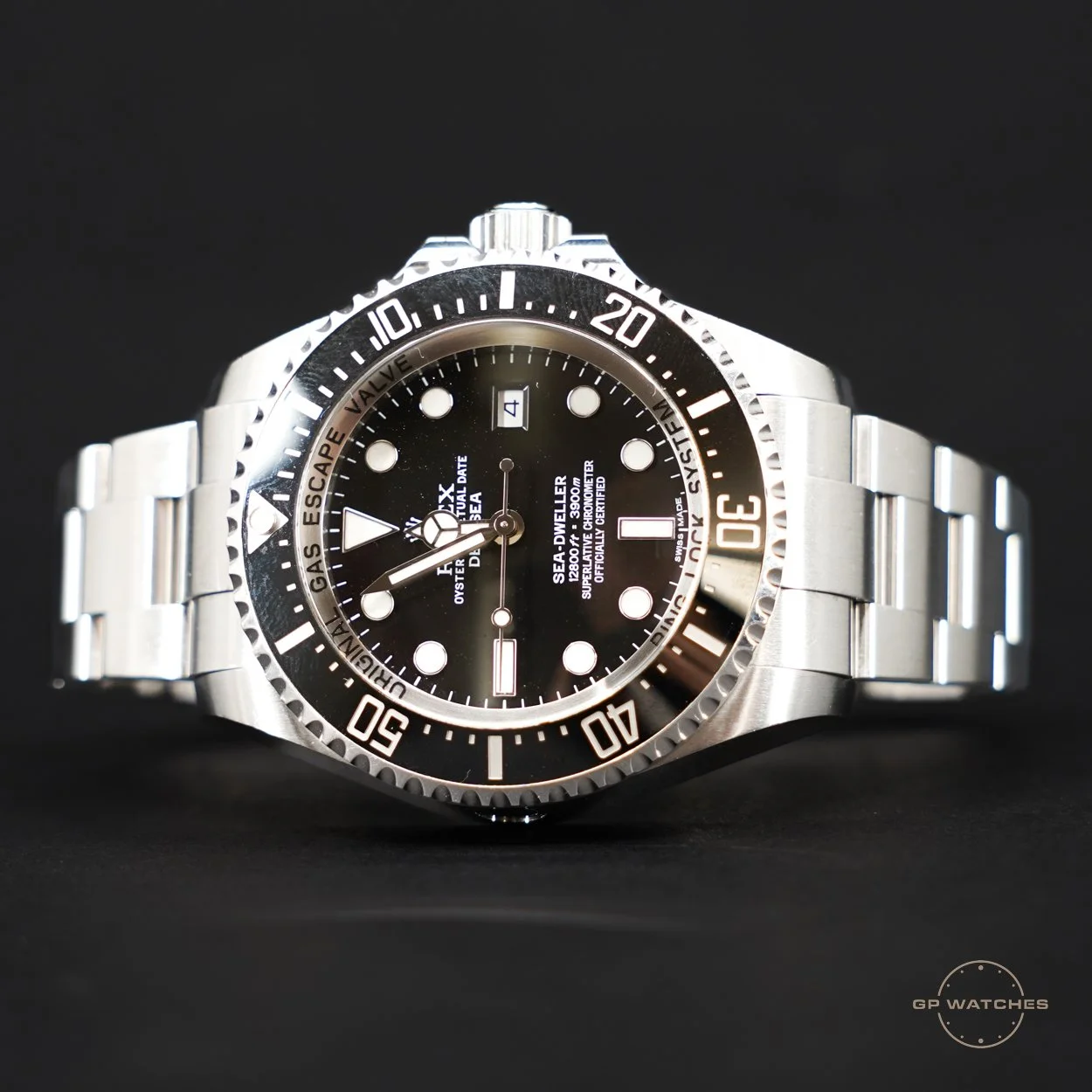 A silver stainless steel wristwatch with a black dial, white hour markers, and a black rotating bezel with white markings, positioned against a black background.