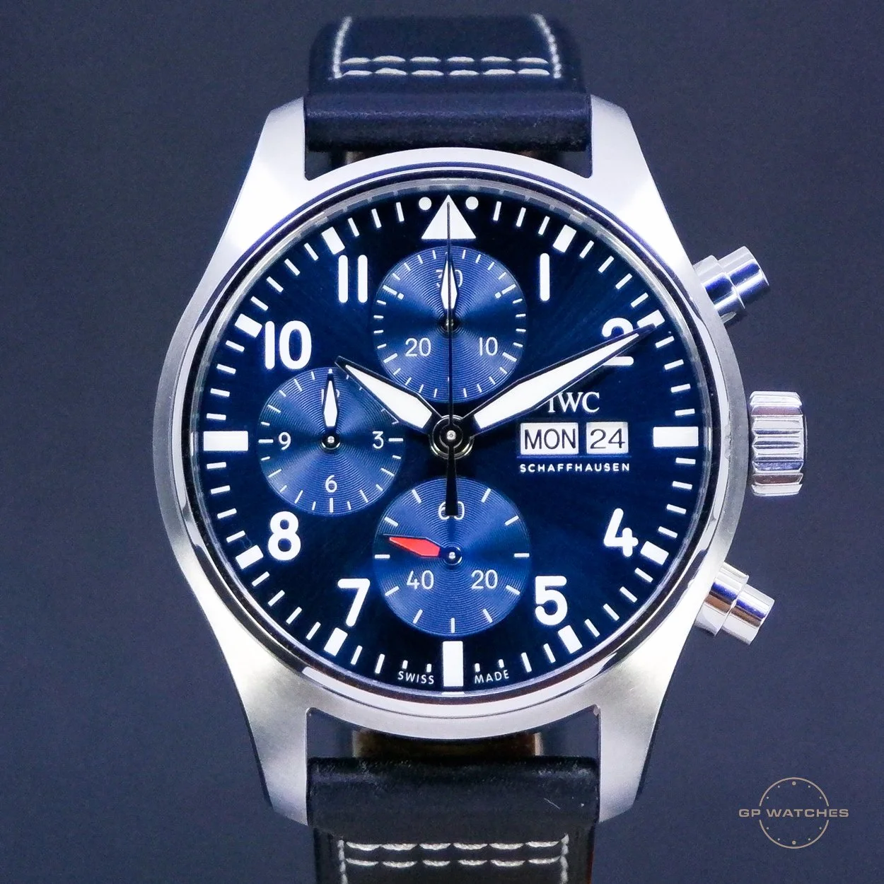 A wristwatch with a blue dial, silver case, and black leather strap. The dial has multiple subdials, a date display, and white numerals and hands.