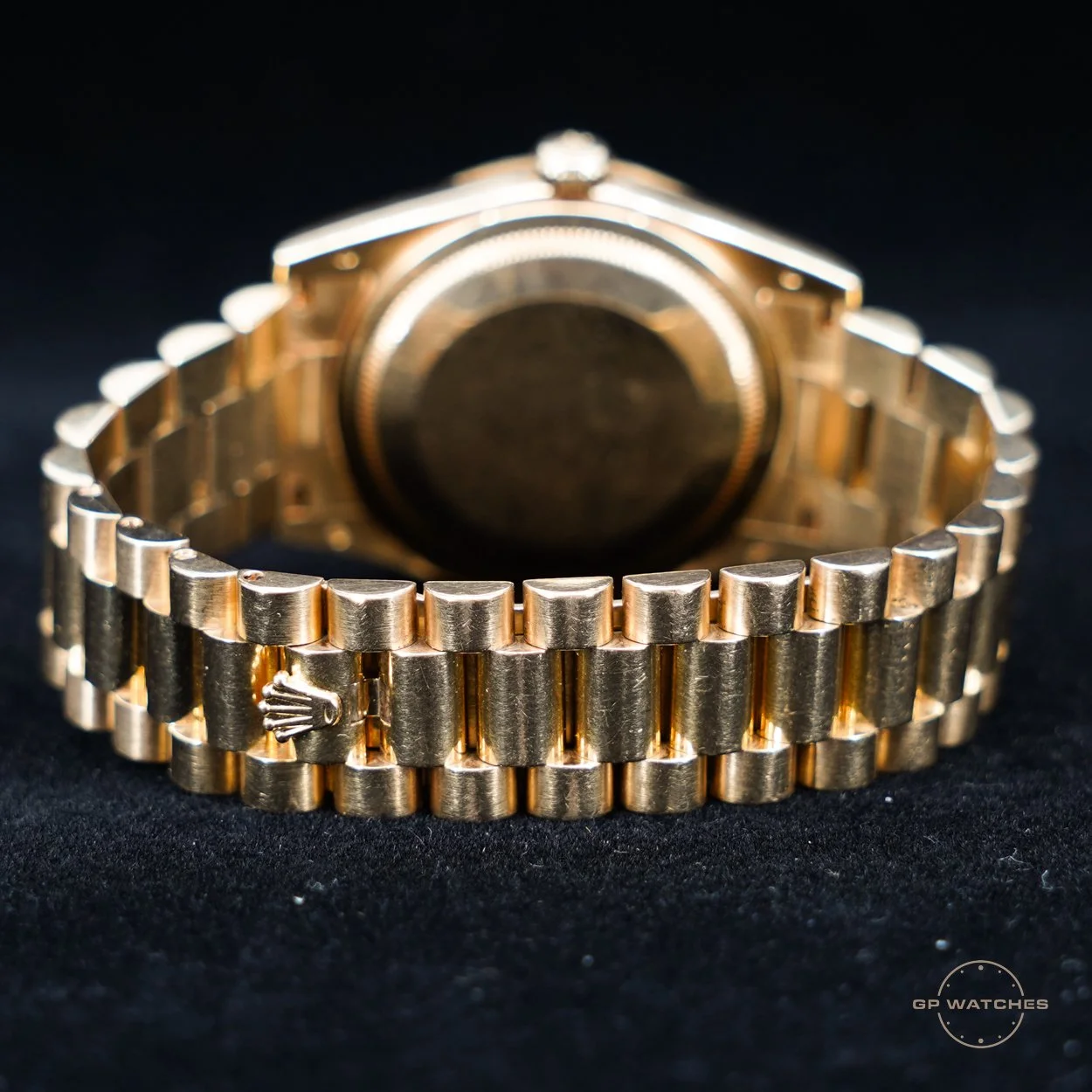 Close-up of a gold wristwatch with a metal band, showing the back case and bracelet against a black background.