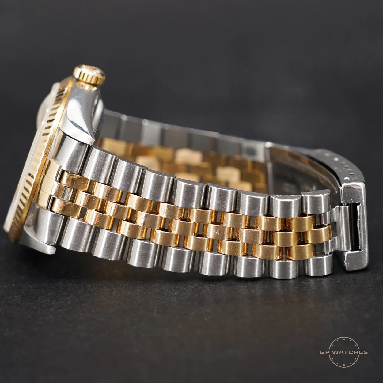 Close-up of a two-tone stainless steel and gold wristwatch with a metal bracelet, showing the side view of the watch case and band against a dark background.