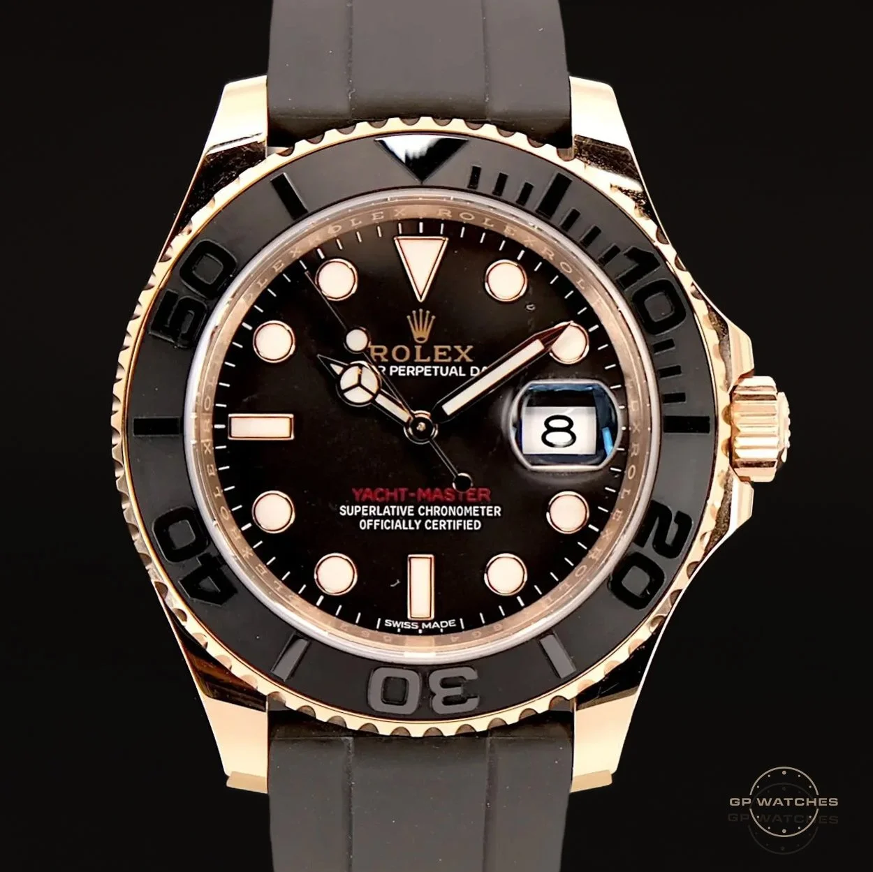 Close-up of a Rolex Yacht-Master watch with black dial, gold bezel, and black strap, showing the date as the 8th.