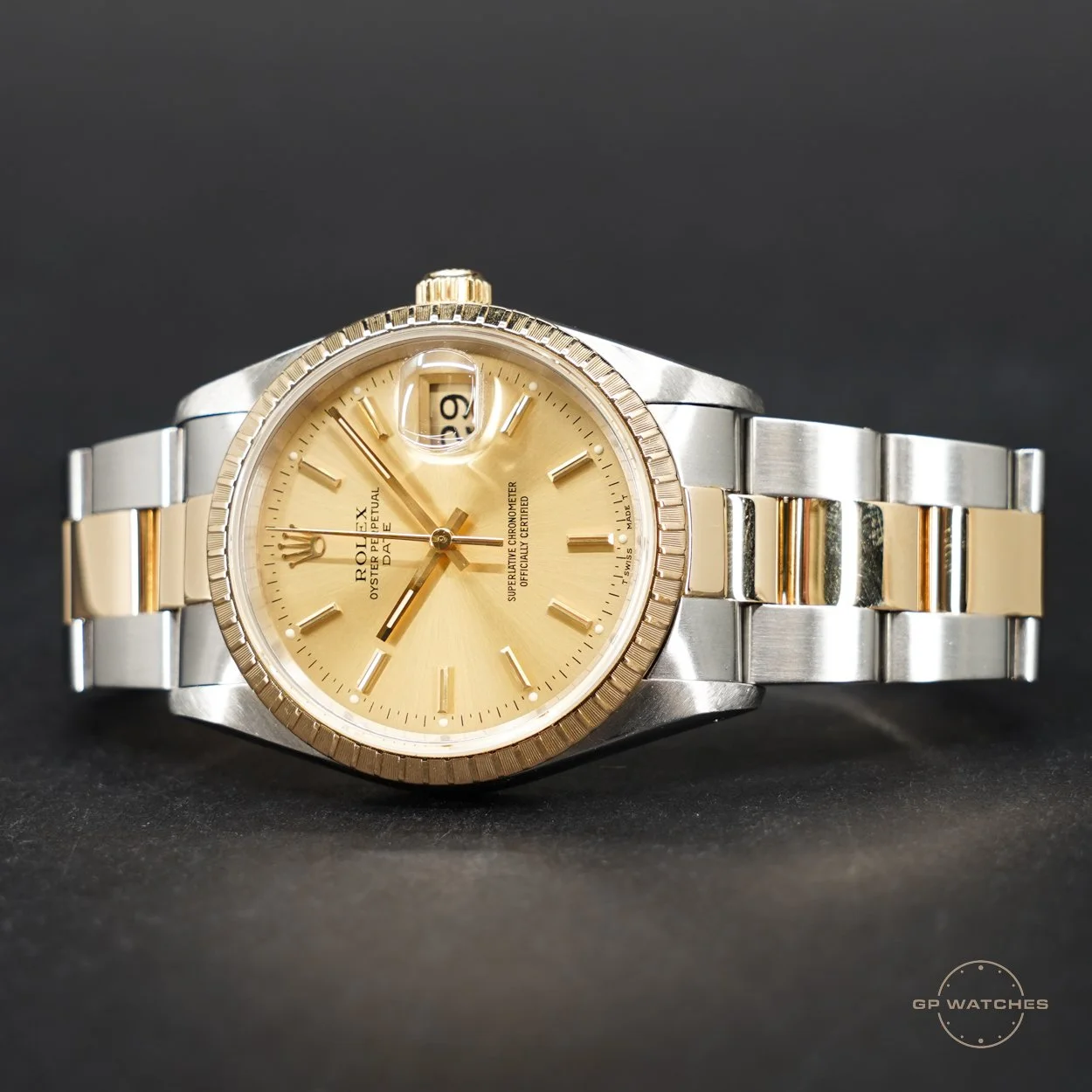 A Rolex Oyster Perpetual Datejust wristwatch with a gold dial, gold and stainless steel band, and a date window at 3 o'clock with a magnifying lens, placed on a black surface.
