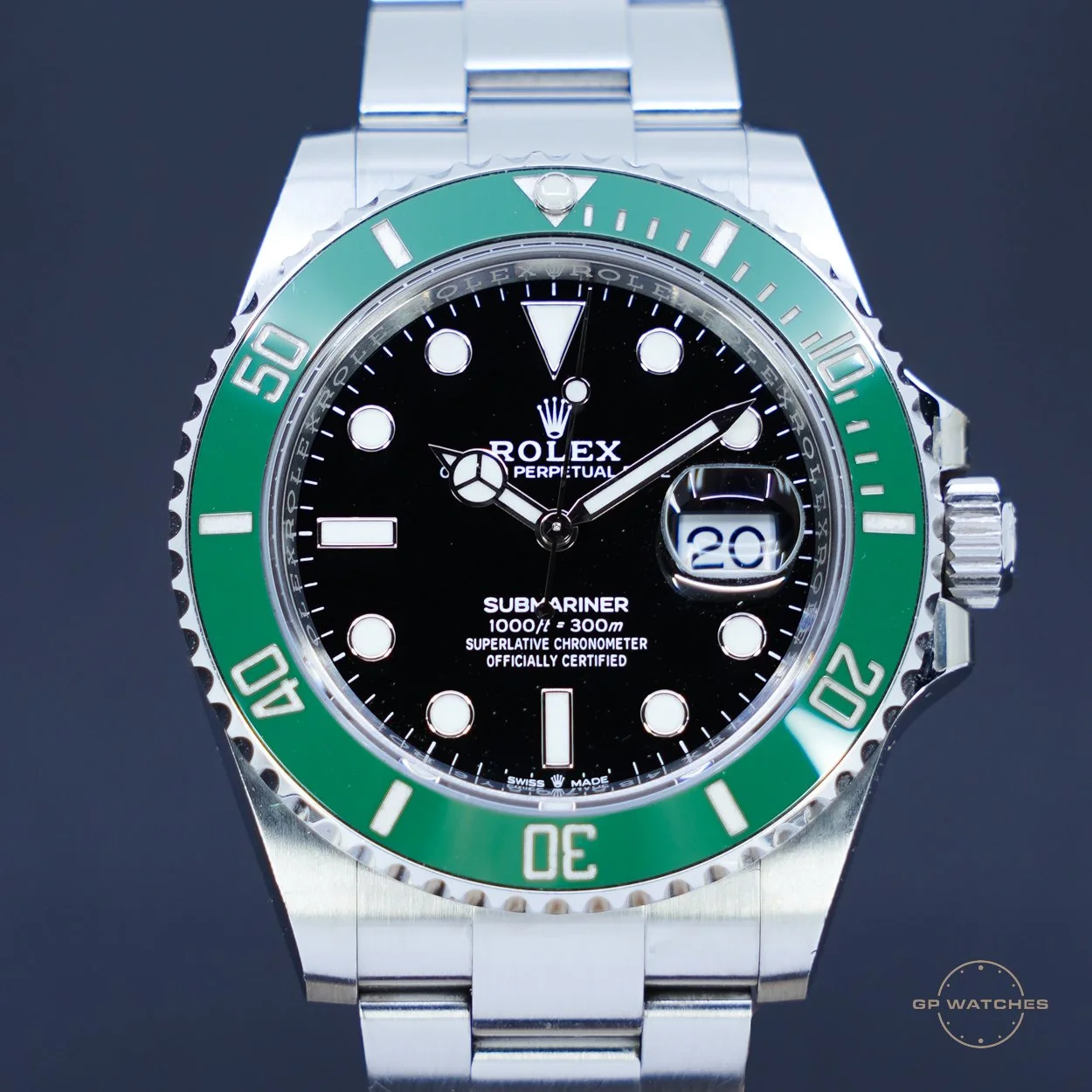 Close-up of a Rolex Submariner watch with a black dial, green bezel, date display at 3 o'clock, and stainless steel bracelet.