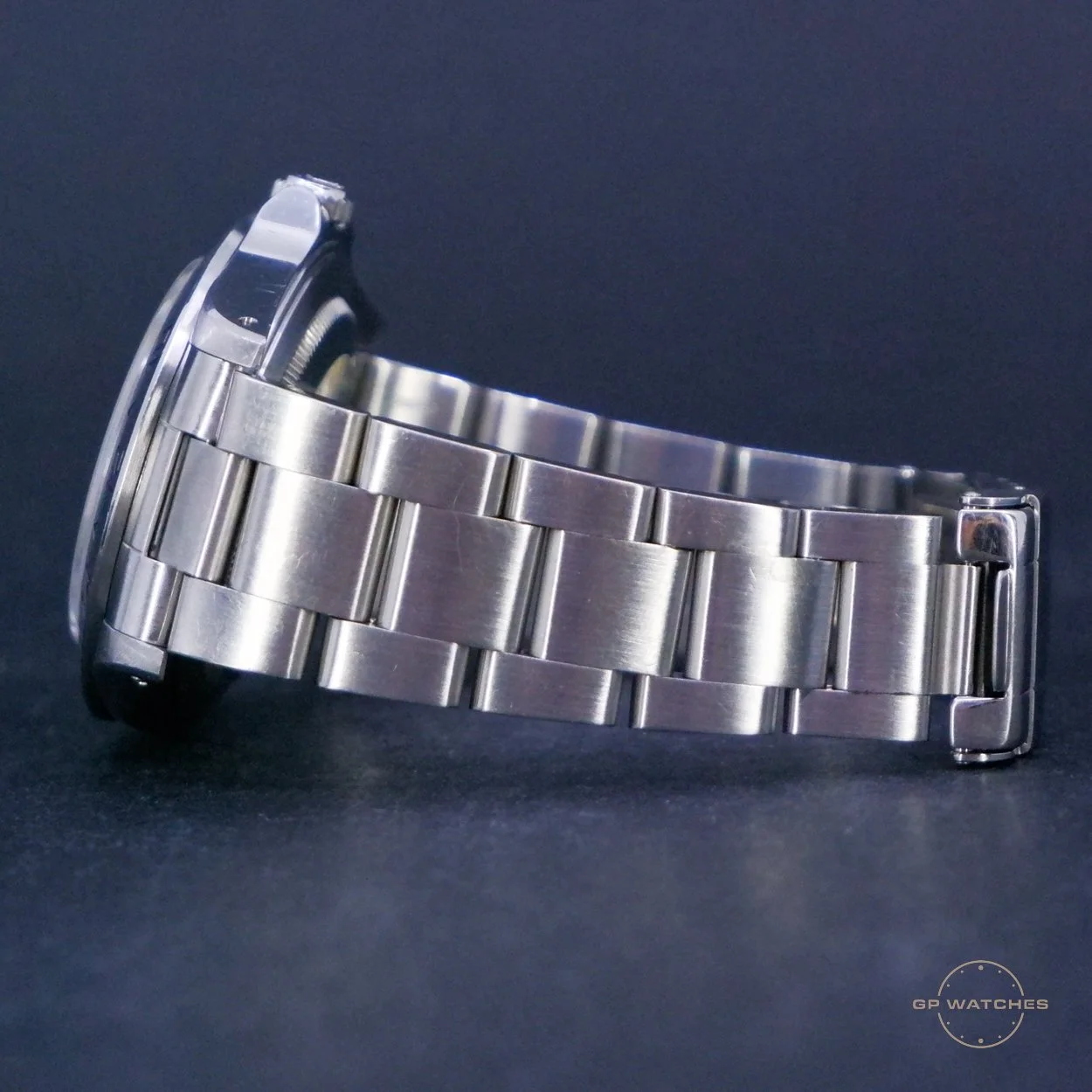 A silver metal wristwatch with a metal link band, laying on a dark surface. The watch face is not visible as the watch is positioned sideways.