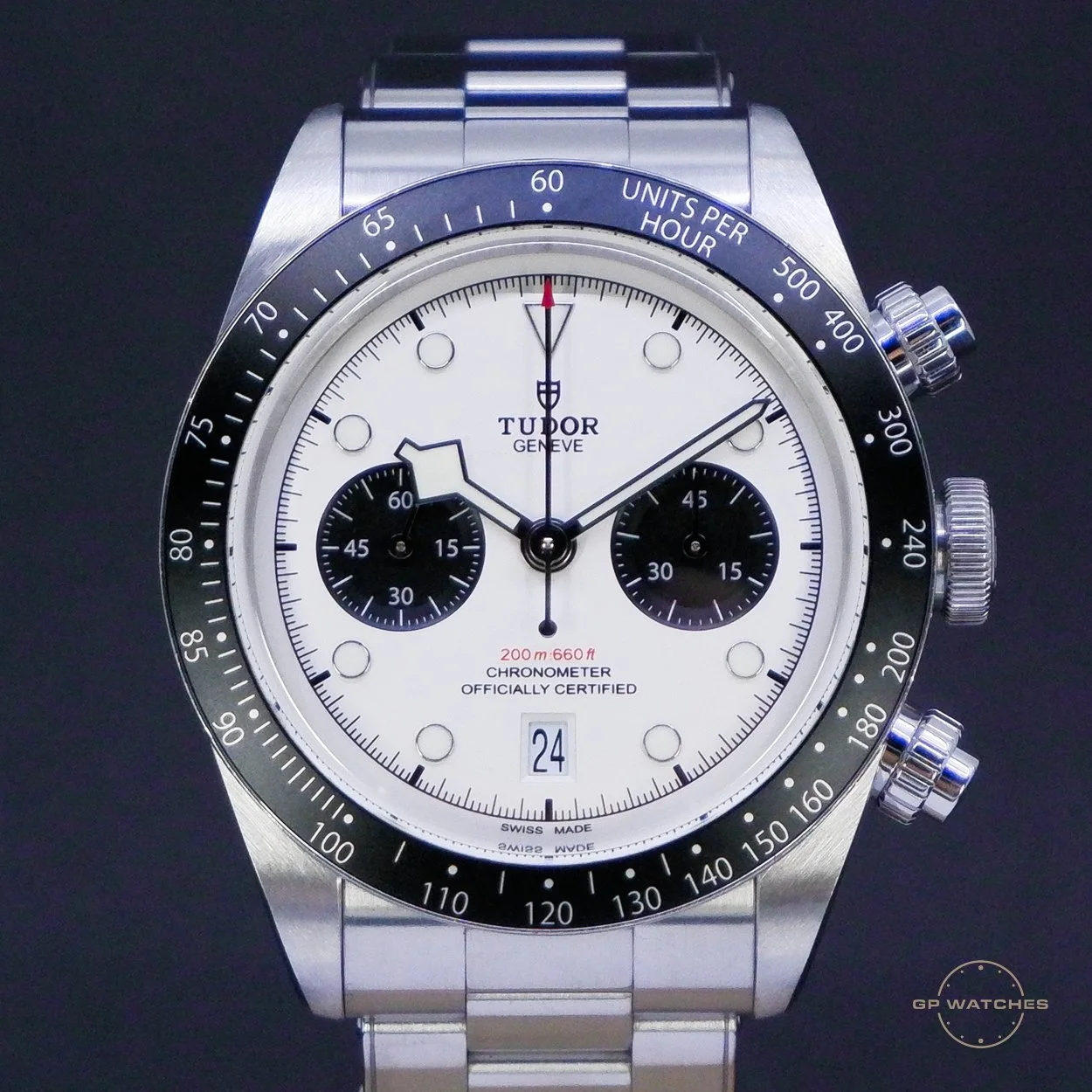 A Tudor Geneva men's wristwatch with a white dial, black subdials, and a stainless steel bracelet. It has chronograph functions, a date window at 6 o'clock, and a tachymeter scale on the bezel.