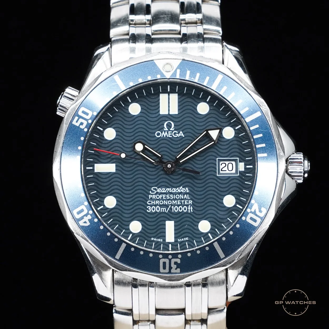 A silver Omega Seamaster Professional chronometer wristwatch with a blue bezel and a dark blue dial. It features white hour markers, a date window at 3 o'clock, and a metal bracelet. The watch also has a unidirectional rotating bezel with minute markers and luminous hands.