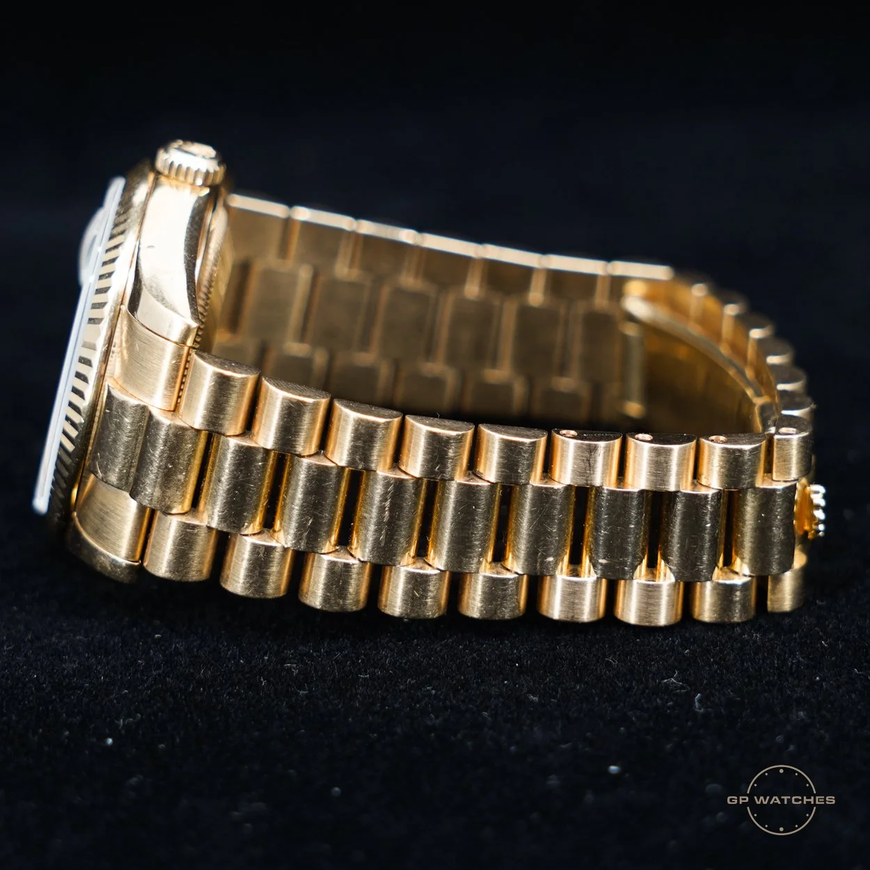 A close-up of a gold metal wristwatch with a textured bezel and a linked gold band, placed on a black surface.
