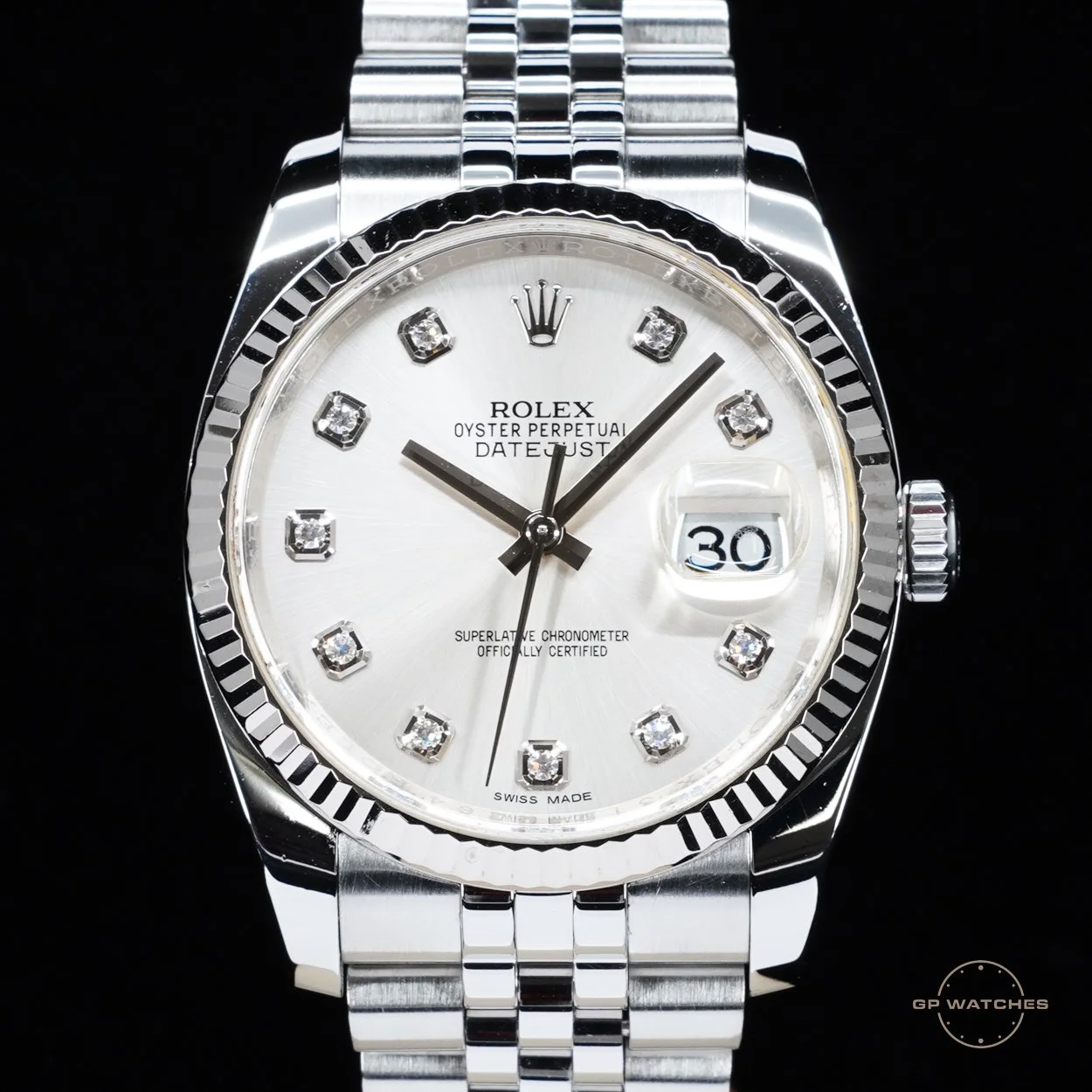 A close-up of a Rolex Oyster Perpetual Datejust wristwatch with a white face, diamond hour markers, and a date window showing the number 30, on a silver metal band against a black background.
