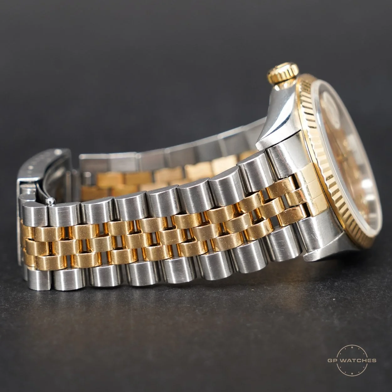 Close-up of a two-tone metal wristwatch with silver and gold links on a dark background.