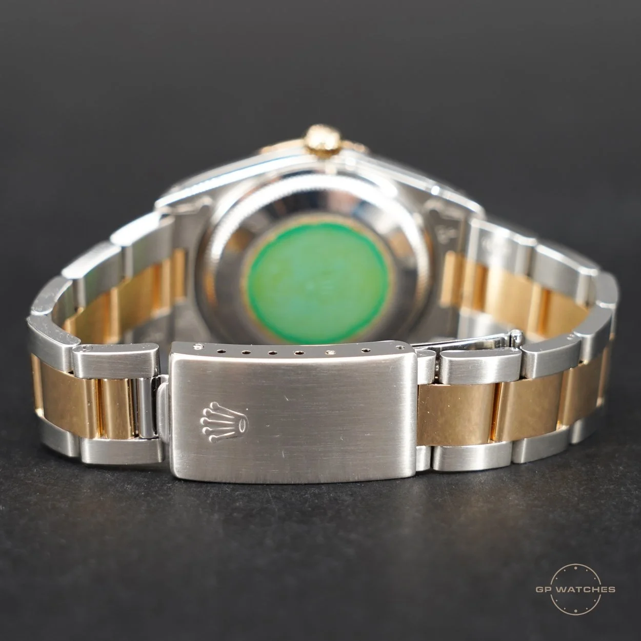 Close-up of a two-tone Rolex watch with a steel and gold bracelet, view of the clasp with Rolex crown logo, and the green holographic sticker on the back of the watch case.