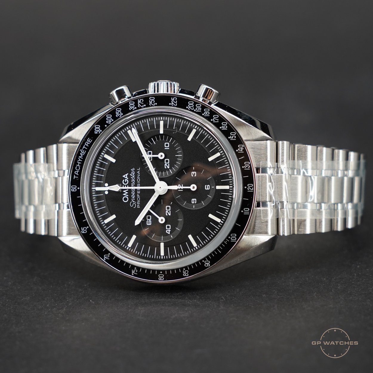 A silver stainless steel Omega Speedmaster Professional chronograph watch with a black dial, white and silver hands, and a tachymeter bezel, displayed against a dark background.