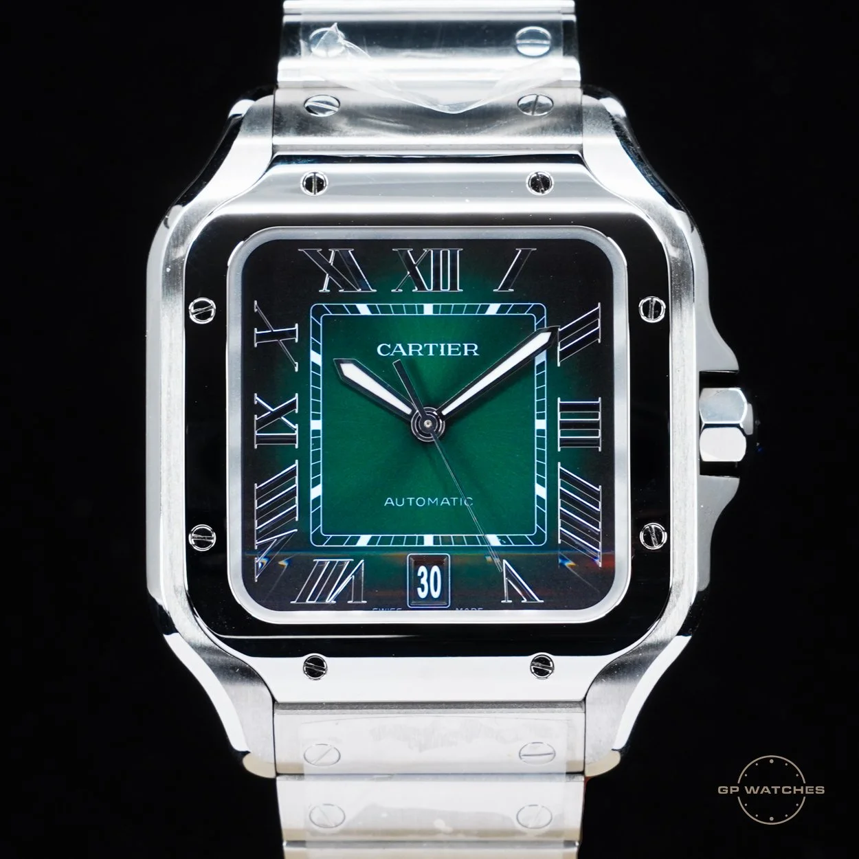A luxury Cartier wristwatch with a green dial, Roman numeral hour markers, and a date window at 6 o'clock. The watch has a square face with a silver metal case and band, and features an automatic movement.
