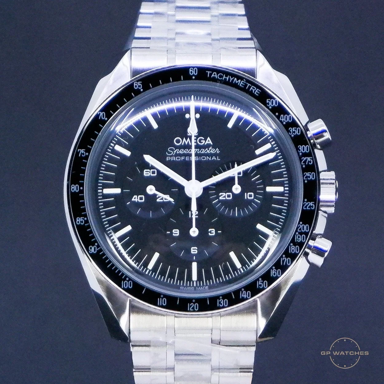 Close-up of an Omega Speedmaster Professional watch with a black dial and silver metal band, showing chronograph subdials and tachymeter scale.