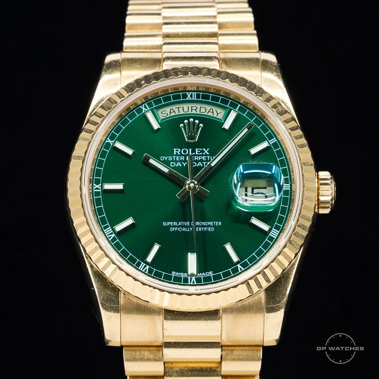 A gold Rolex watch with a green dial, displaying the day and date, with a fluted bezel and gold bracelet.