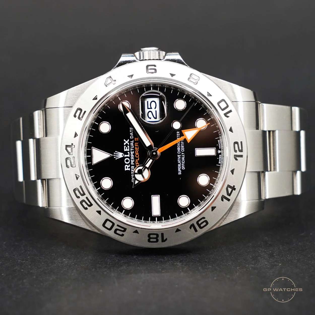 Close-up of a Rolex Explorer II watch with a black dial, silver bezel, and a silver metal band, showing the date at 3 o'clock and orange 24-hour hand.