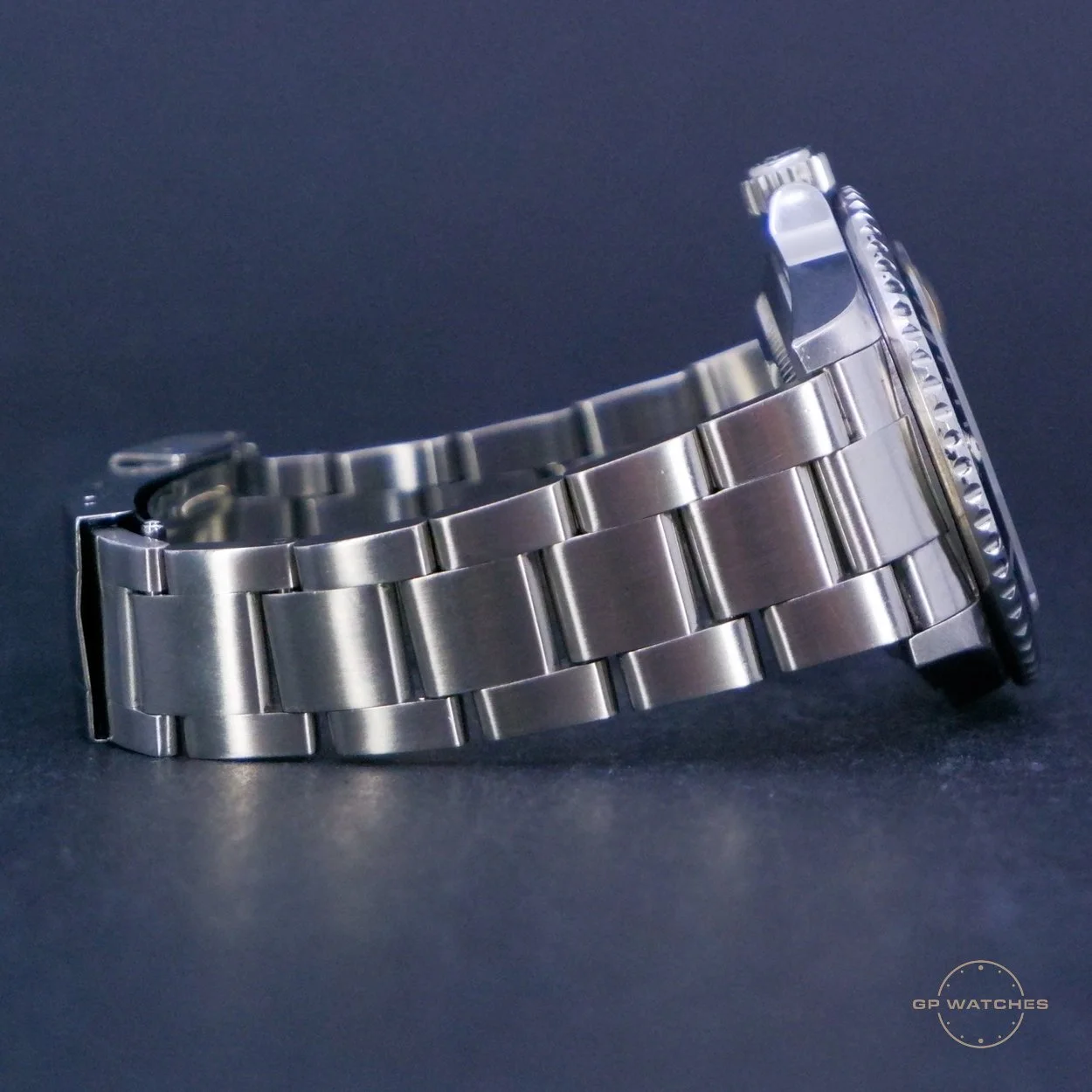 A stainless steel wristwatch with a metal band, placed on a dark surface with a faint logo that reads 'GP Watches' in the bottom right corner.