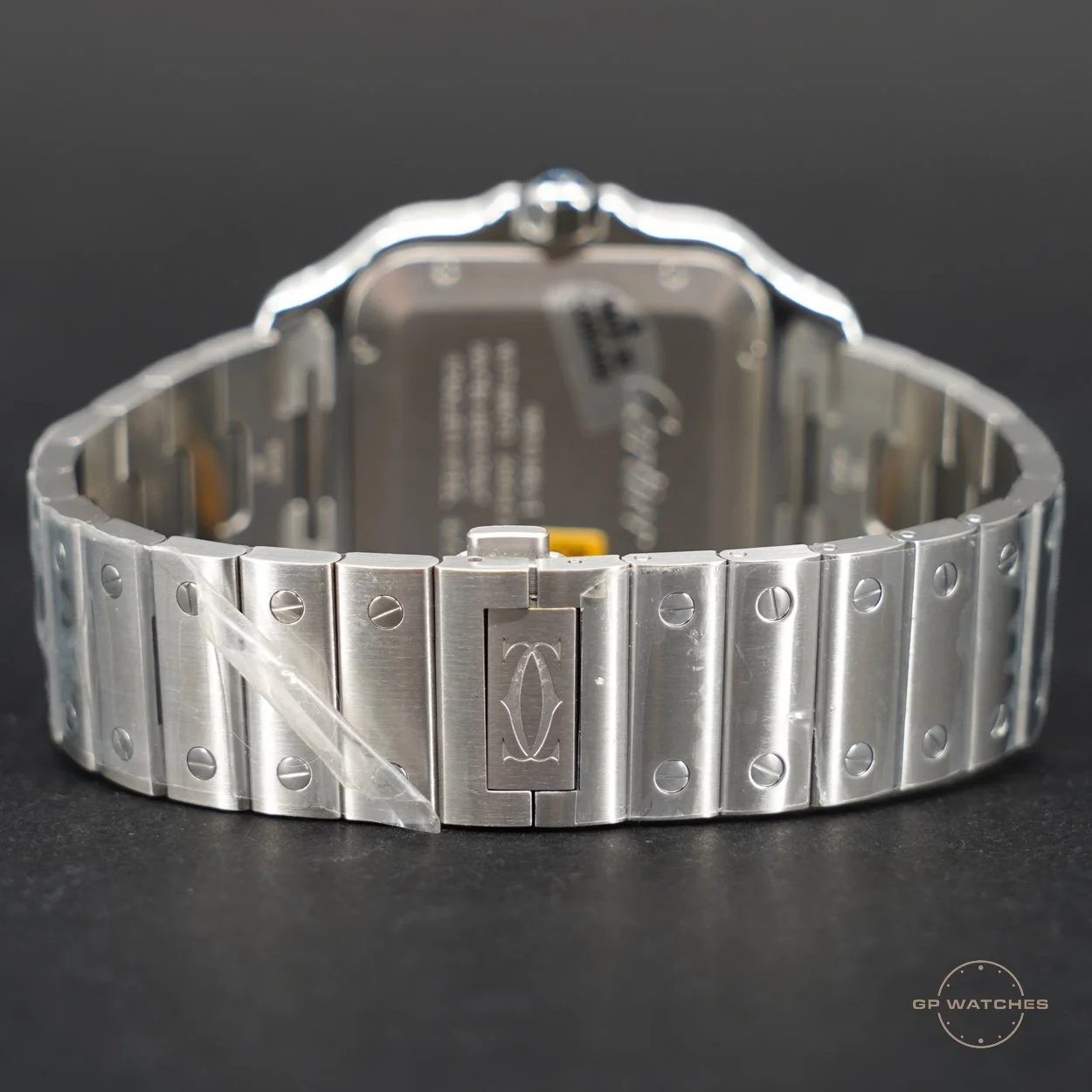 Silver metal wristwatch with a linked band and a clasp featuring a logo, resting on a black surface