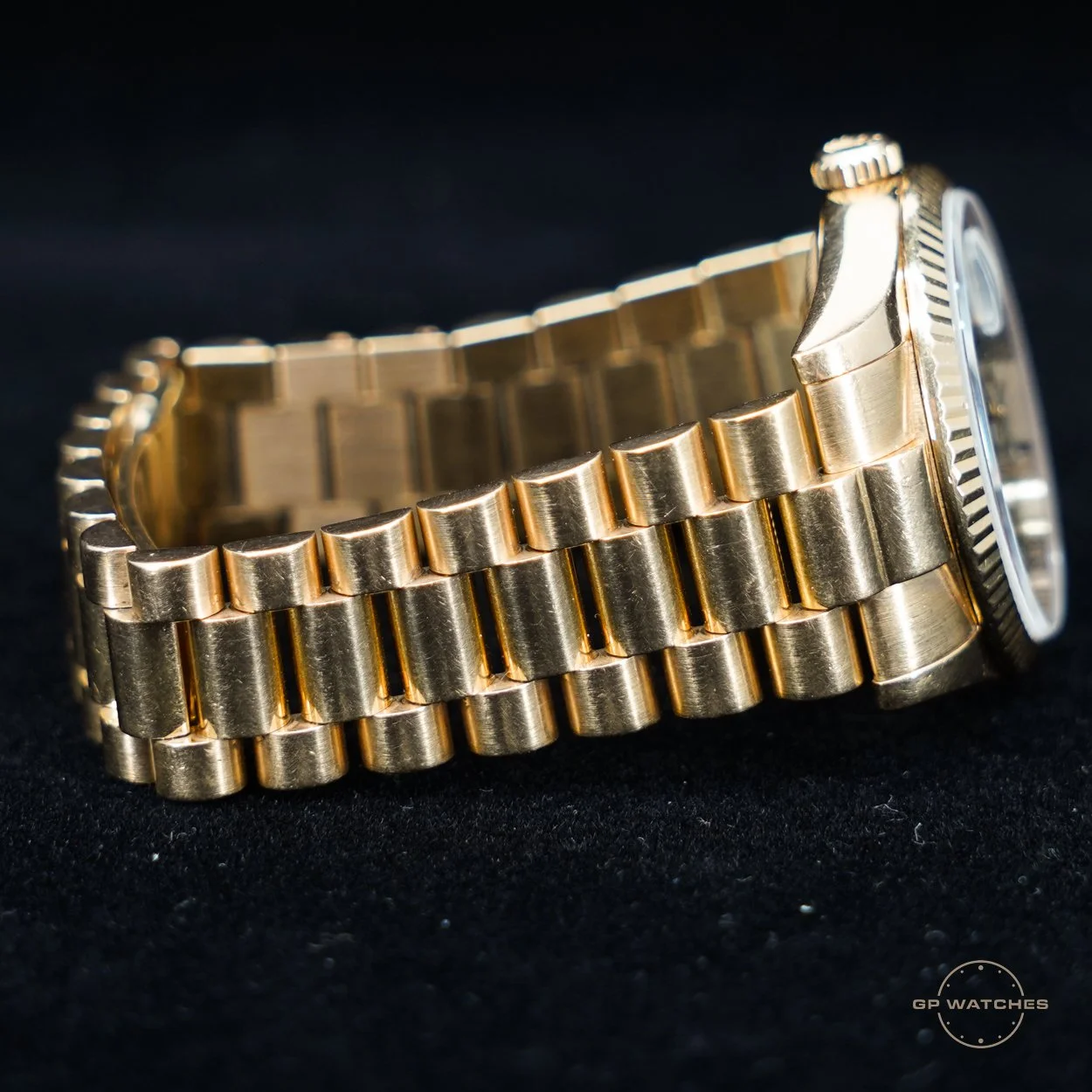 Close-up of a gold wristwatch with a link bracelet, lying on a black surface.