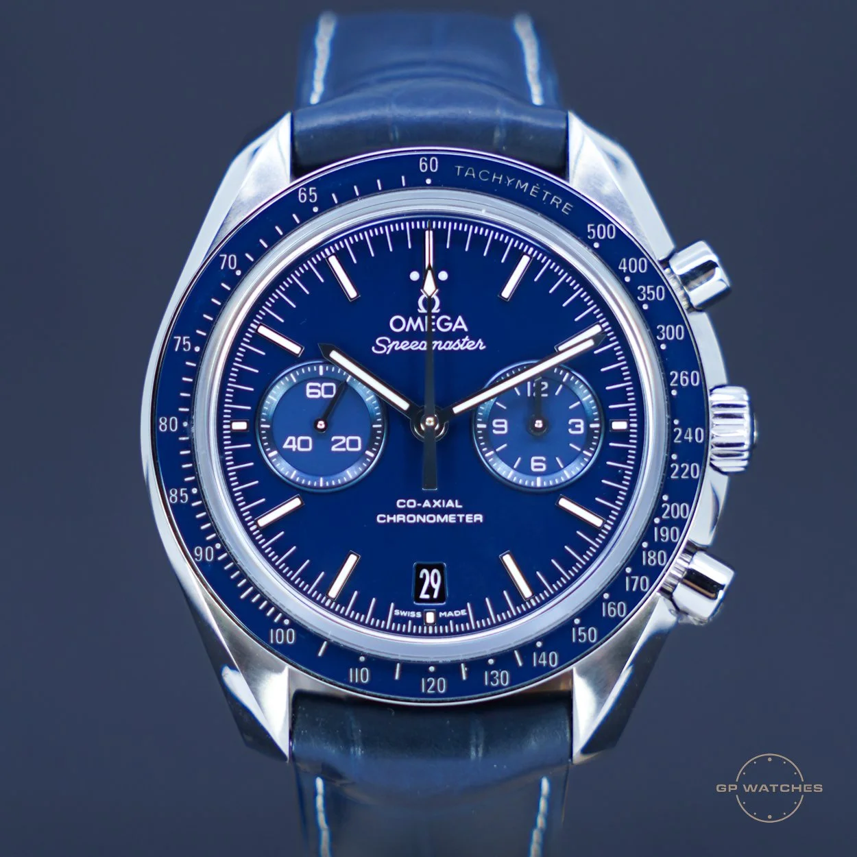 Close-up of an Omega Speedmaster wristwatch with a blue dial, black leather strap, and chronograph features.