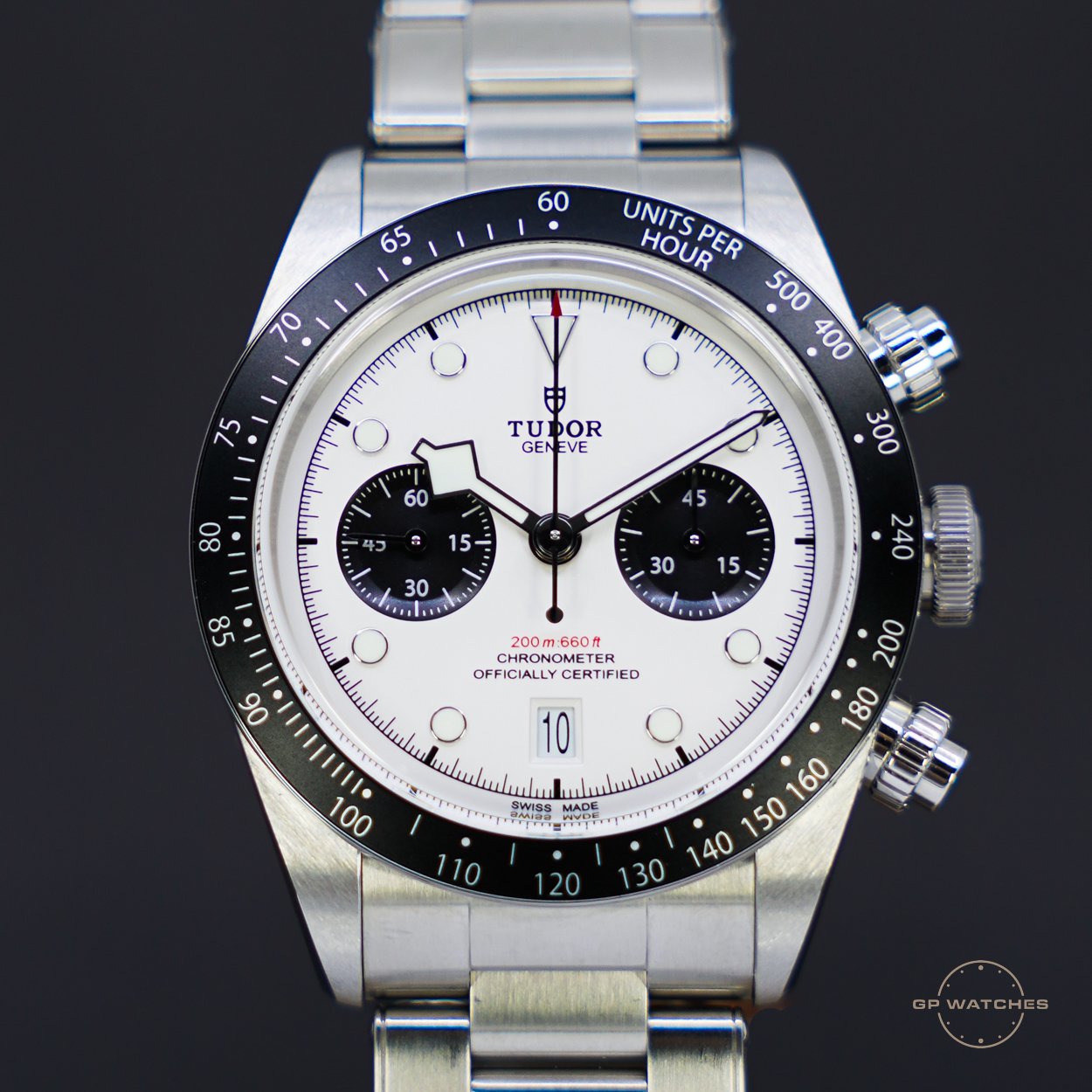 A Tudor Geneve chronograph watch with a white dial, black subdials, and a black tachymeter bezel, featuring a date window at 6 o'clock and three pushers on the side.