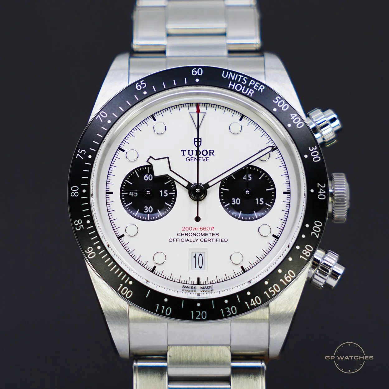 A stainless steel Tudor chronograph watch with a white dial, black subdials, and a black tachymeter bezel, displaying time, date, and chronograph features.