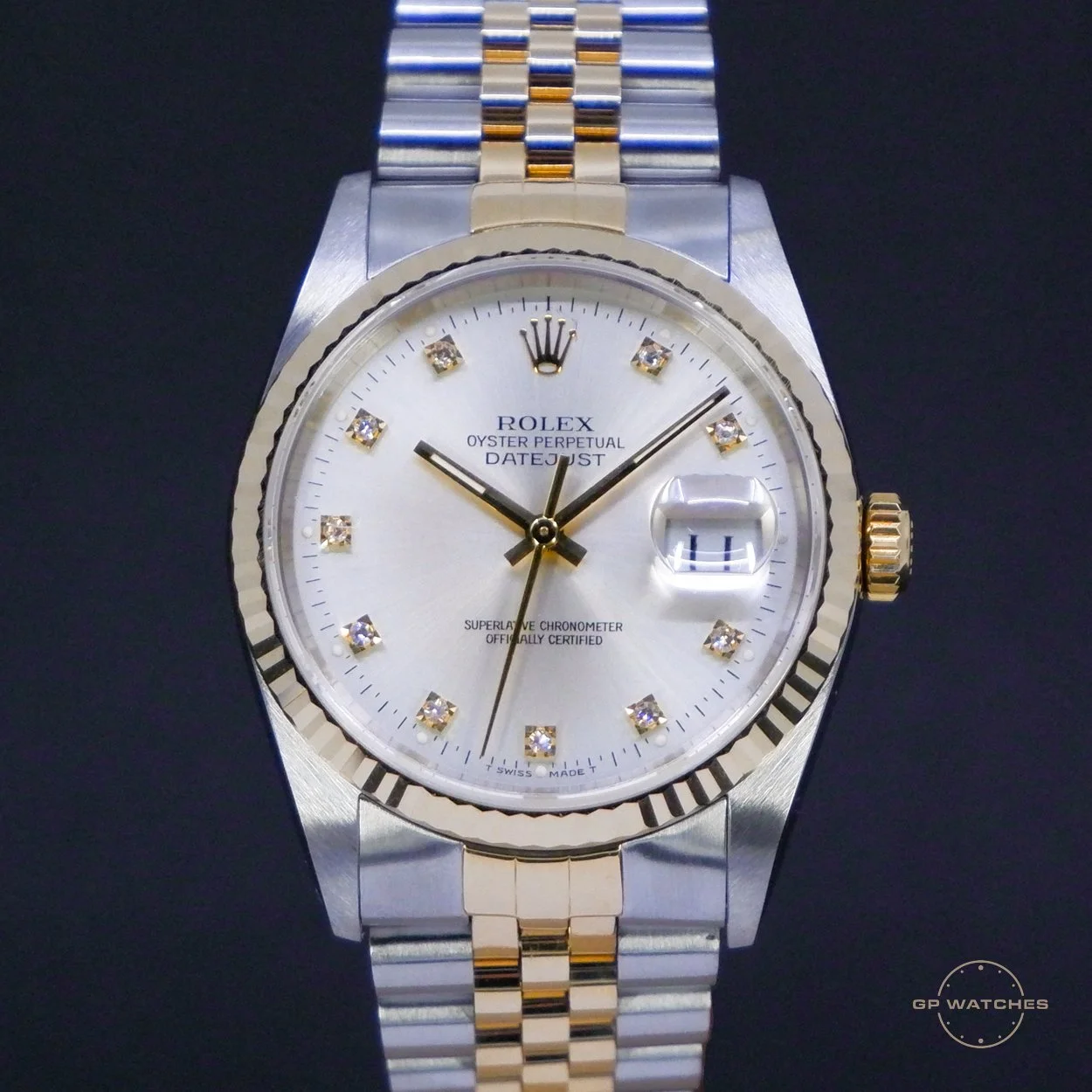 A two-tone Rolex Oyster Perpetual Datejust wristwatch with a silver dial, diamond hour markers, a date display with magnifier at 3 o'clock, and a gold fluted bezel, set against a dark background.