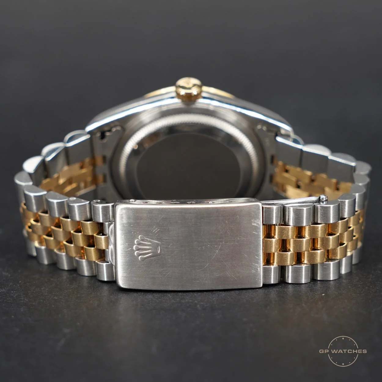 Close-up of a luxury two-tone metal wristwatch with a silver and gold band, showing the back and part of the clasp engraved with a Rolex logo, on a dark background.