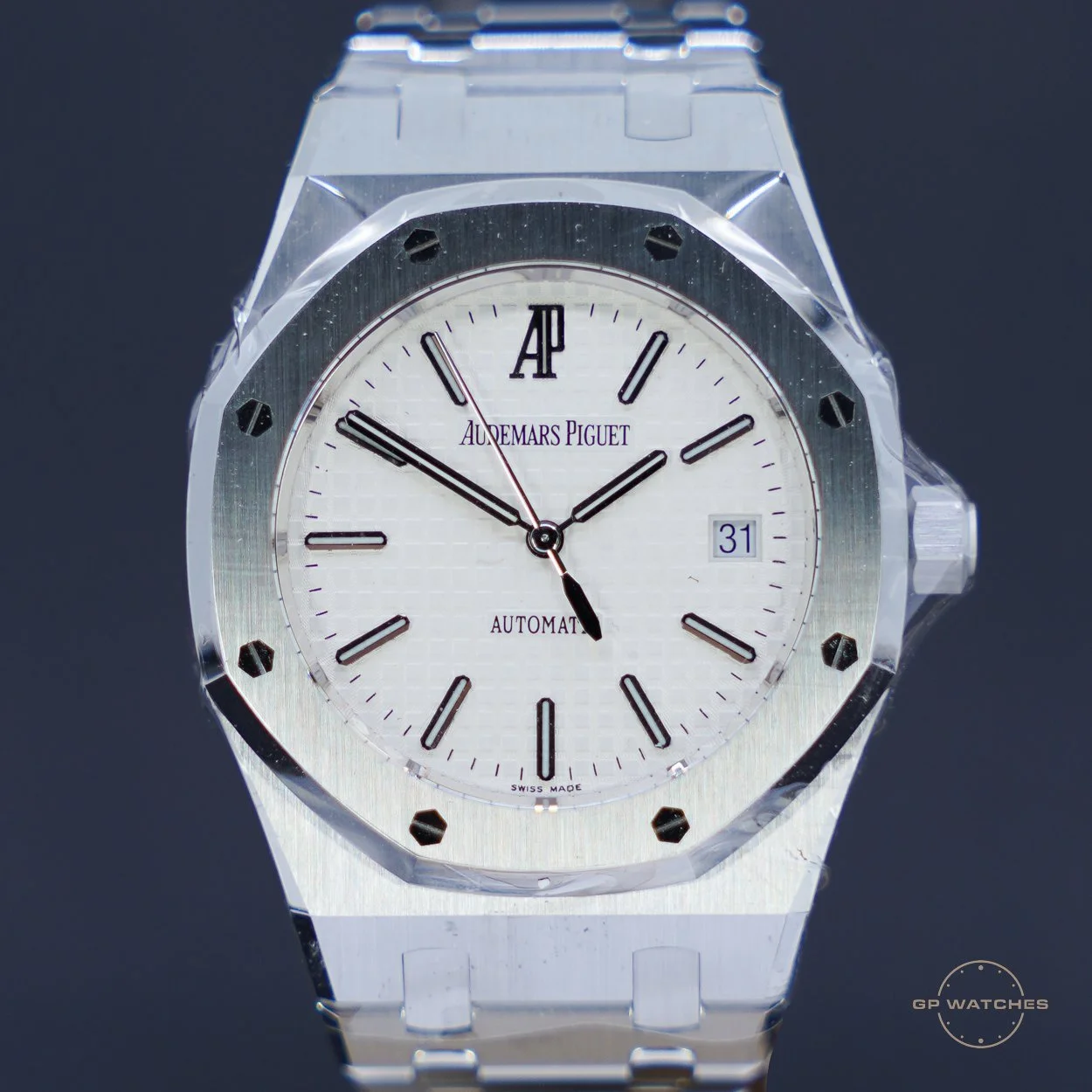 A white luxury wristwatch with a metal band, featuring black hour markers and hands, a date display at 3 o'clock, and the brand name Audemars Piguet on the dial.