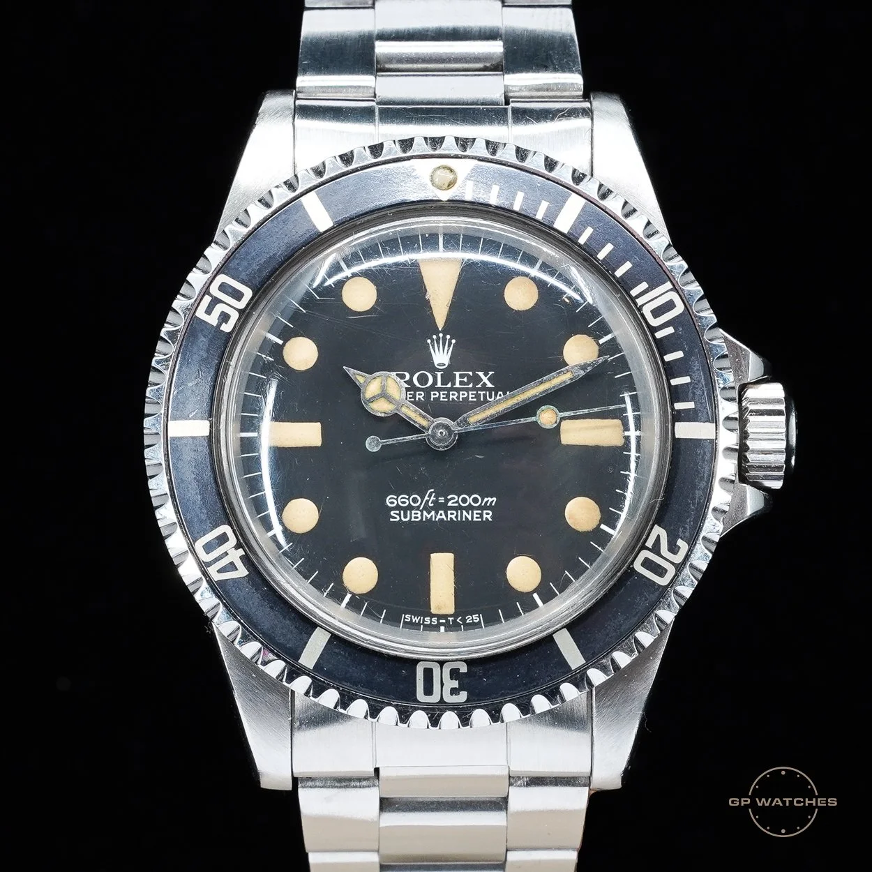 A vintage Rolex Submariner watch with a black dial, beige hour markers, and a stainless steel bracelet, set against a black background.