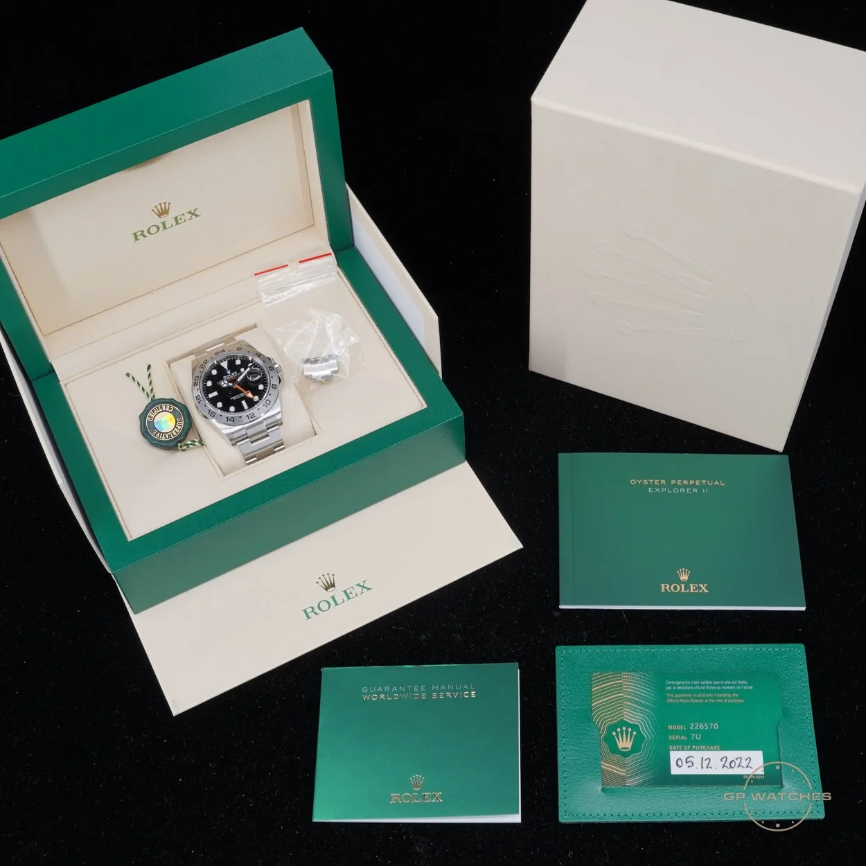 A Rolex wristwatch with a metal band inside its green box, along with accompanying manuals, guarantee card, and tags, all set on a black surface.