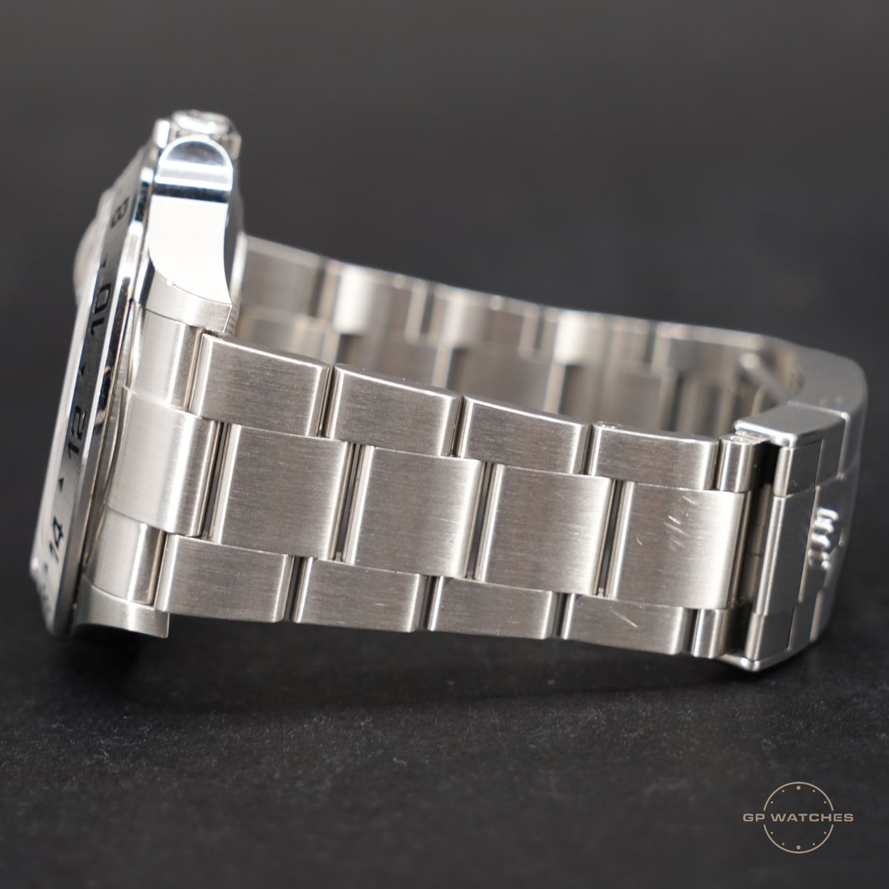 Close-up of a stainless steel wristwatch with a metal link bracelet, shown from the side with a black background.